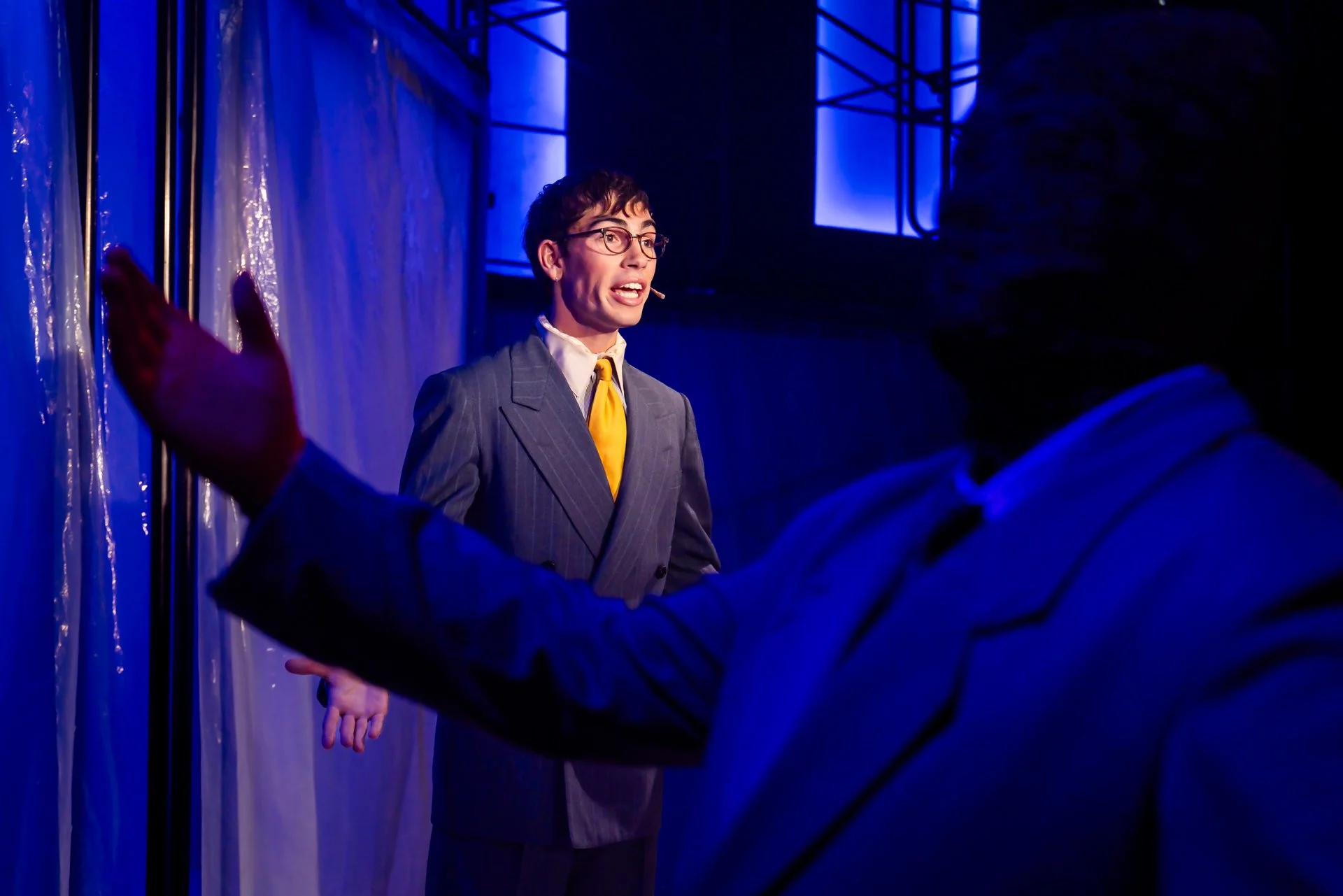 Patrick Bateman in a suit and yellow tie under blue light in American Psycho at Shenandoah Conservatory