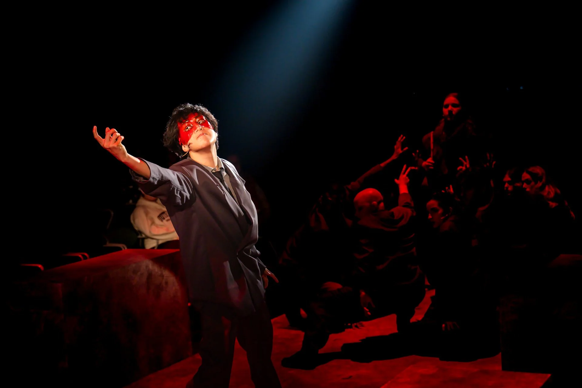 Performer in a blood-splattered mask under a spotlight with the ensemble in American Psycho at Shenandoah Conservatory
