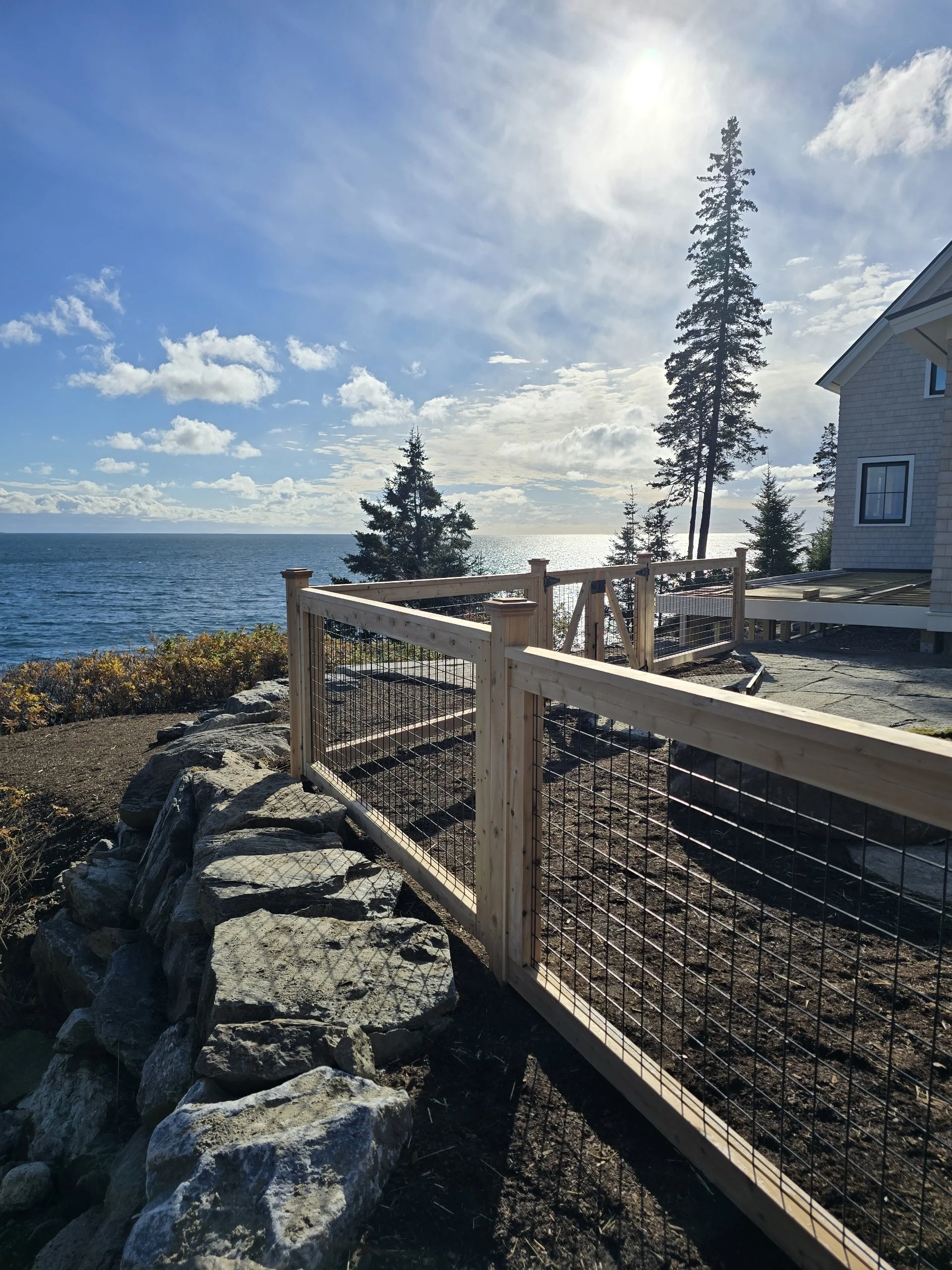 Ocean view Maine rocky landscape with cedar wrapped welded wire fence patio enclosure, house and tree