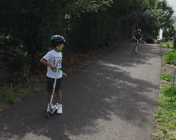 Mike Maddux's sons, Michael and Noah, riding scooters outside.