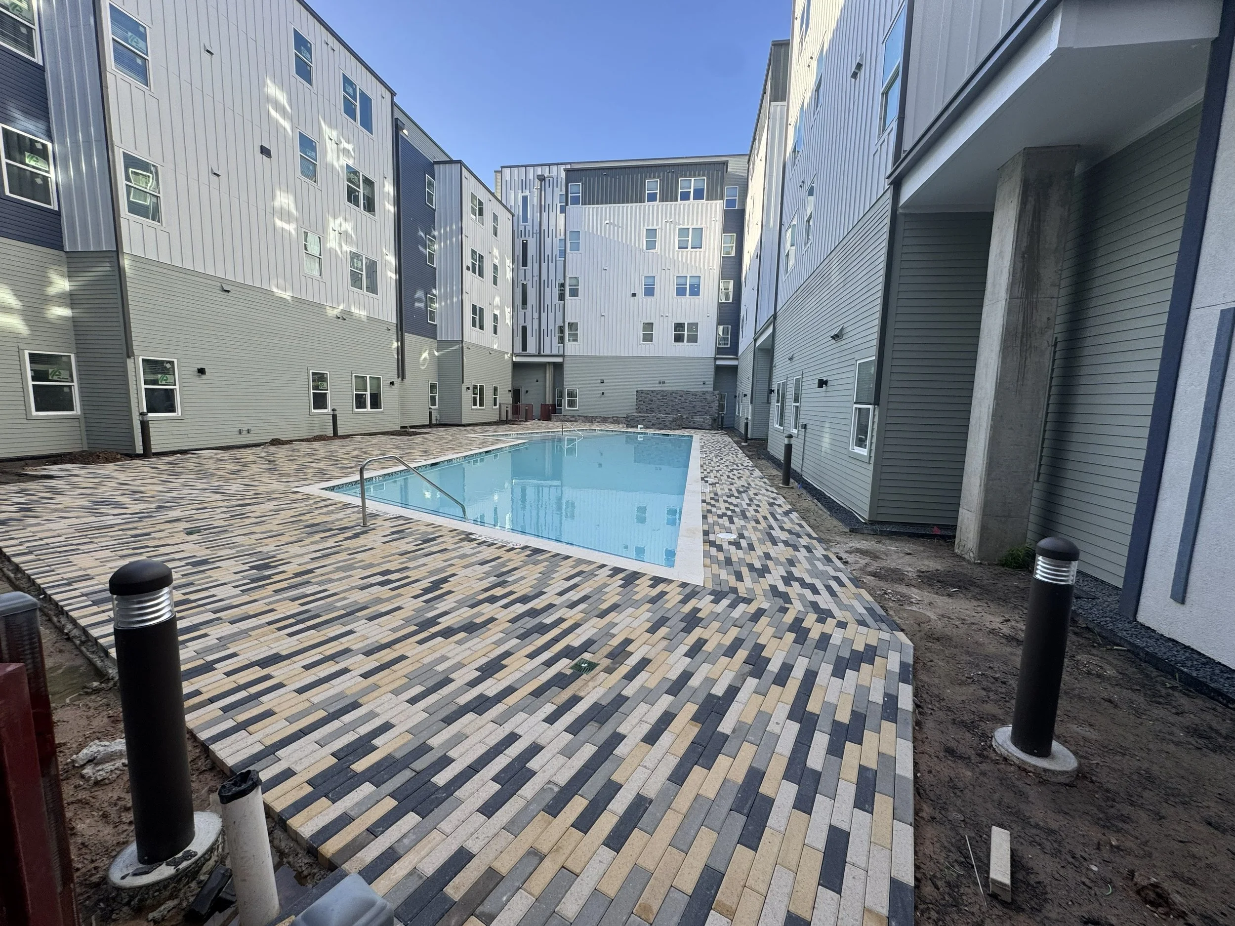 An outdoor courtyard with a swimming pool surrounded by multistory buildings with modern architecture and gray siding, under a clear blue sky.