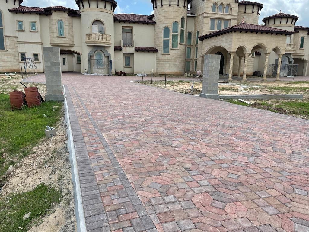 Newly paved brick driveway leading to a large beige castle-like house with rounded towers and arched doorways.