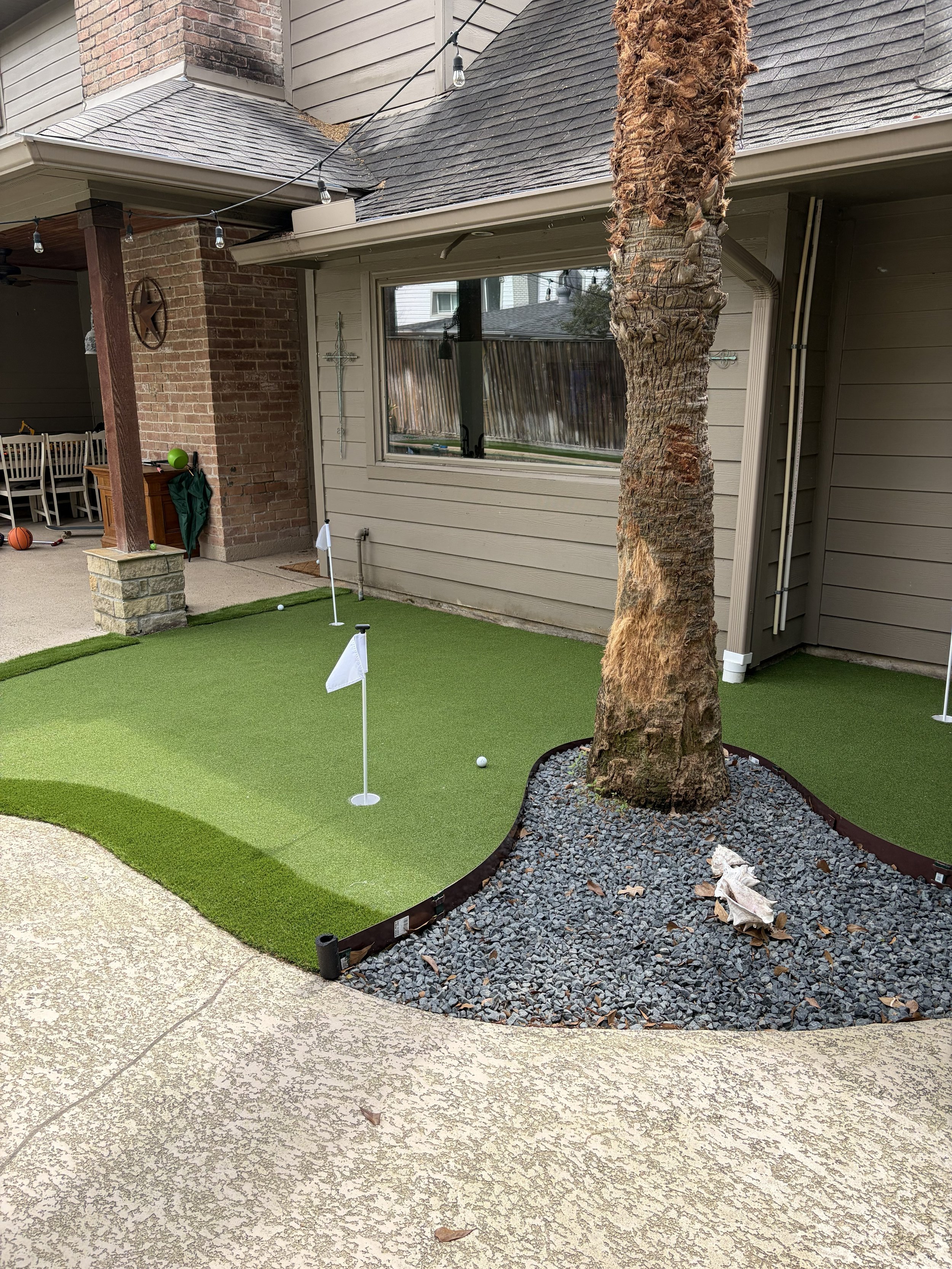 Backyard with putting green, palm tree, string lights, and patio furniture in the background.