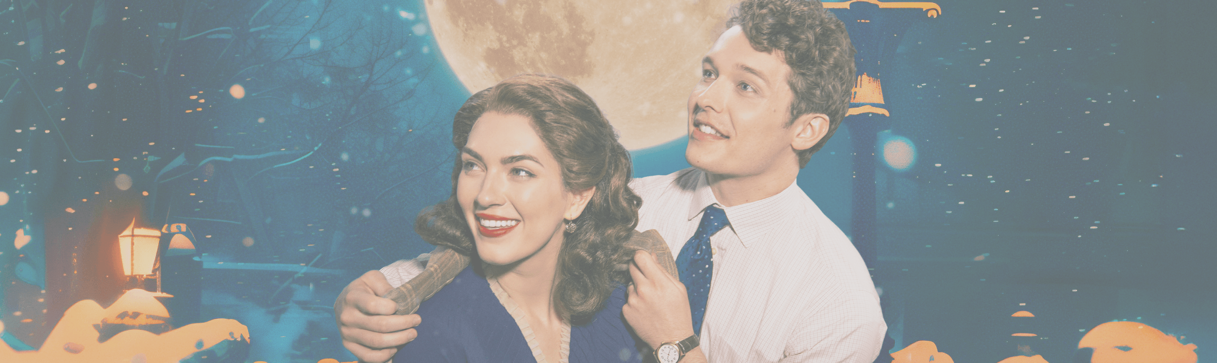 George and Mary from It’s a Wonderful Life stand together outdoors at night as snow falls, illuminated by a glowing streetlamp and a large full moon.