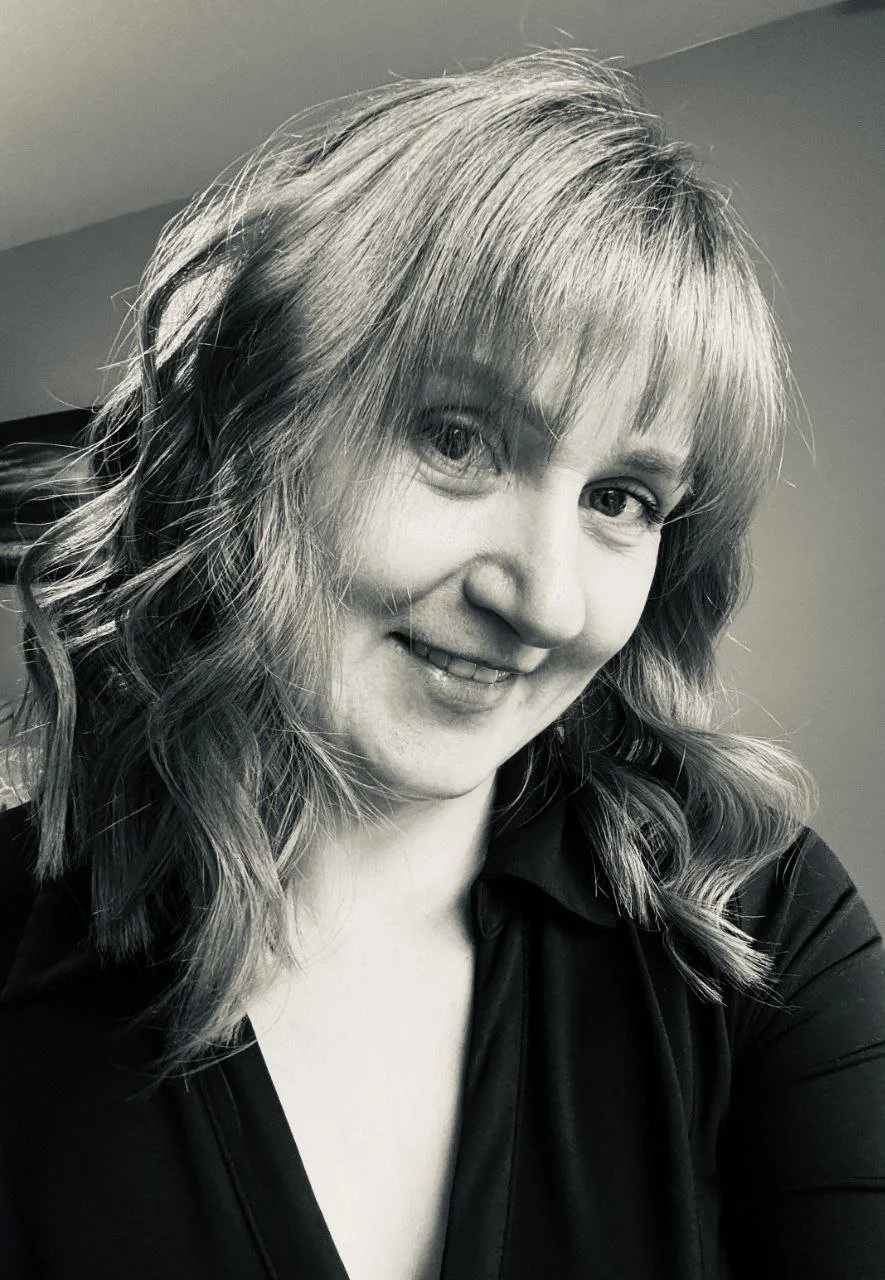 Black and white photo of a woman with shoulder-length wavy hair, smiling, wearing a dark top.