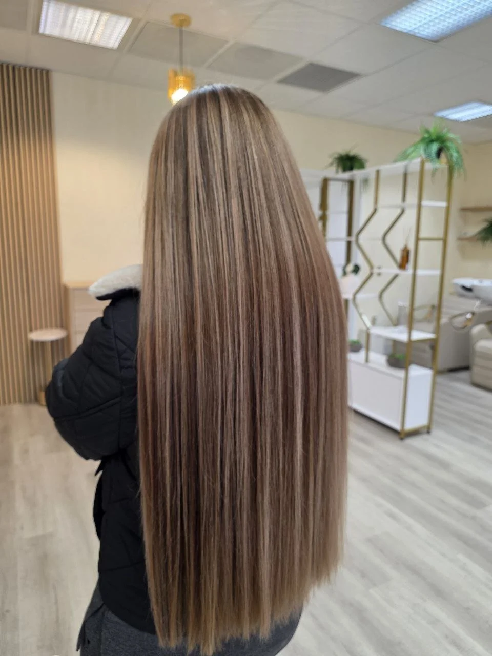 Back view of a woman with long, straight, light brown hair in a salon.