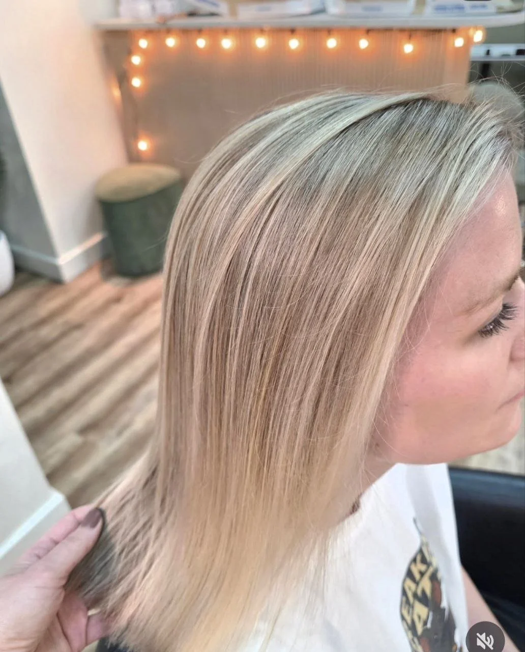 Close-up of a woman's blonde, straight, shiny hair in a salon or studio setting.