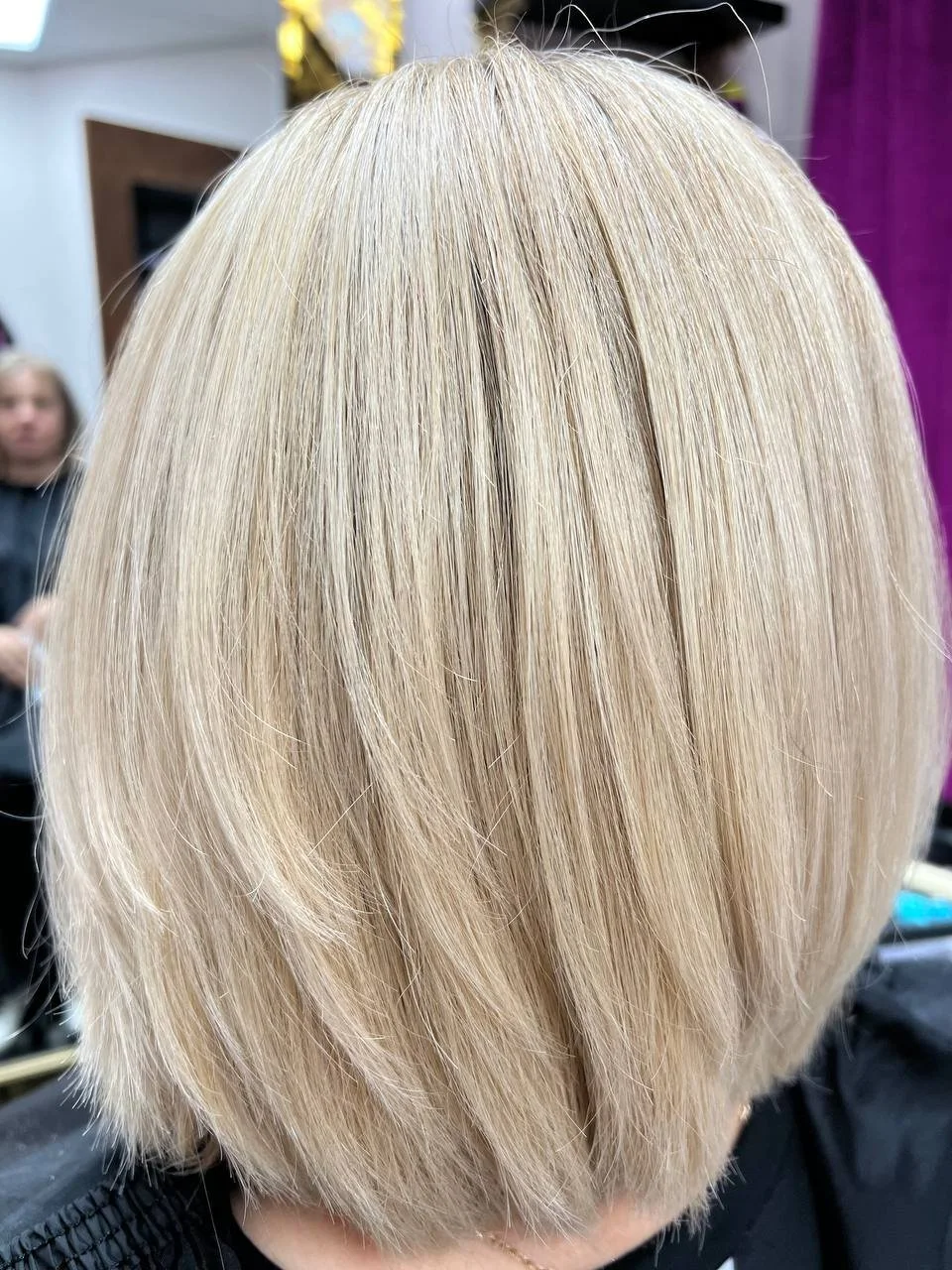 Blonde bob haircut on a person in a salon, with a mirror and other salon equipment visible in the background.