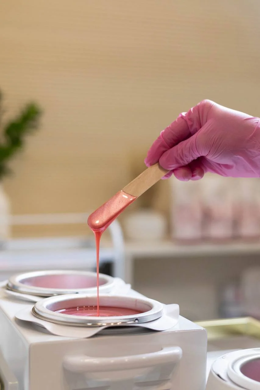 A gloved hand dipping a wooden stick into pink nail polish