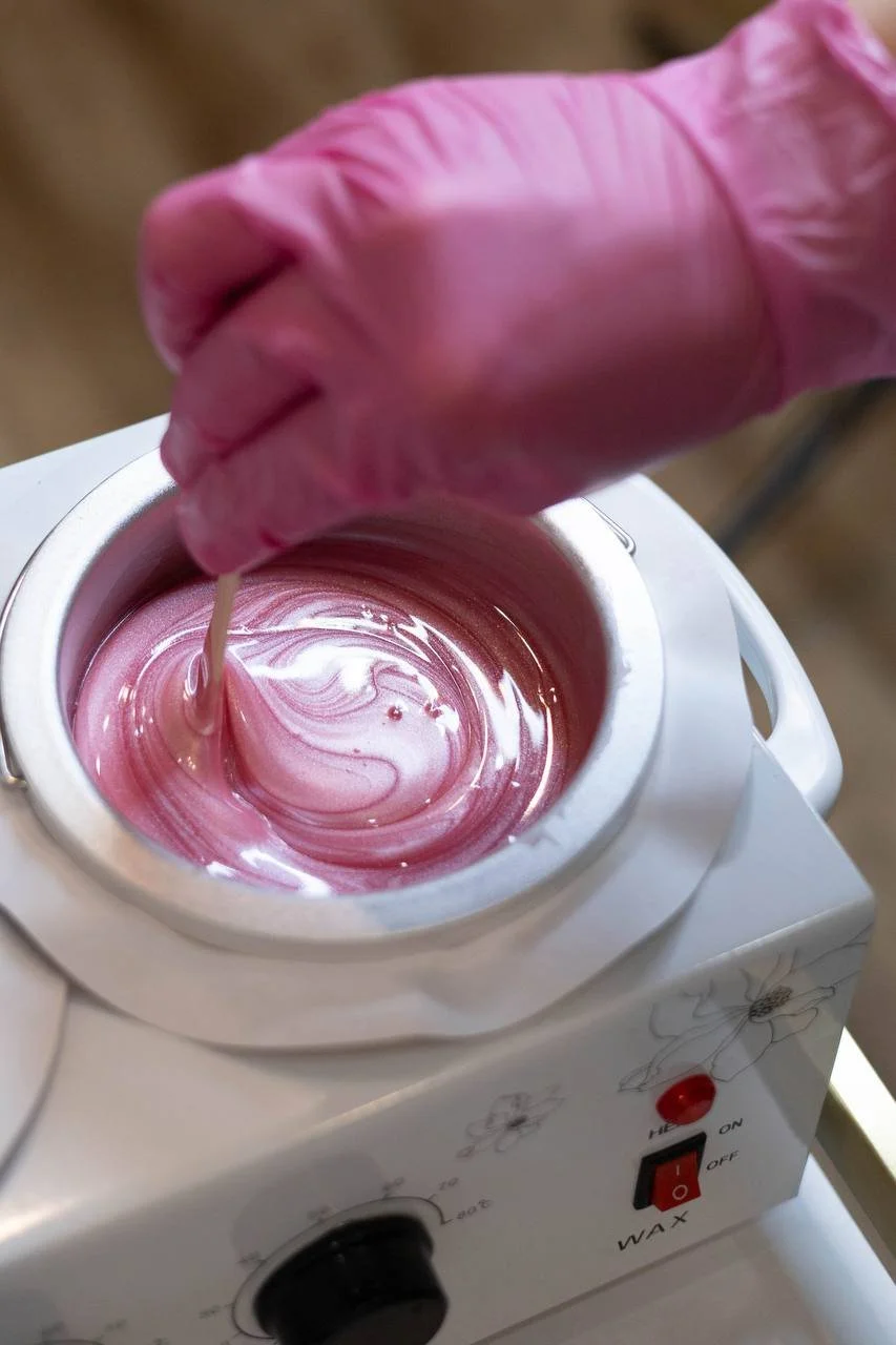 Pink wax being melted in a wax warmer by hand wearing a pink glove.