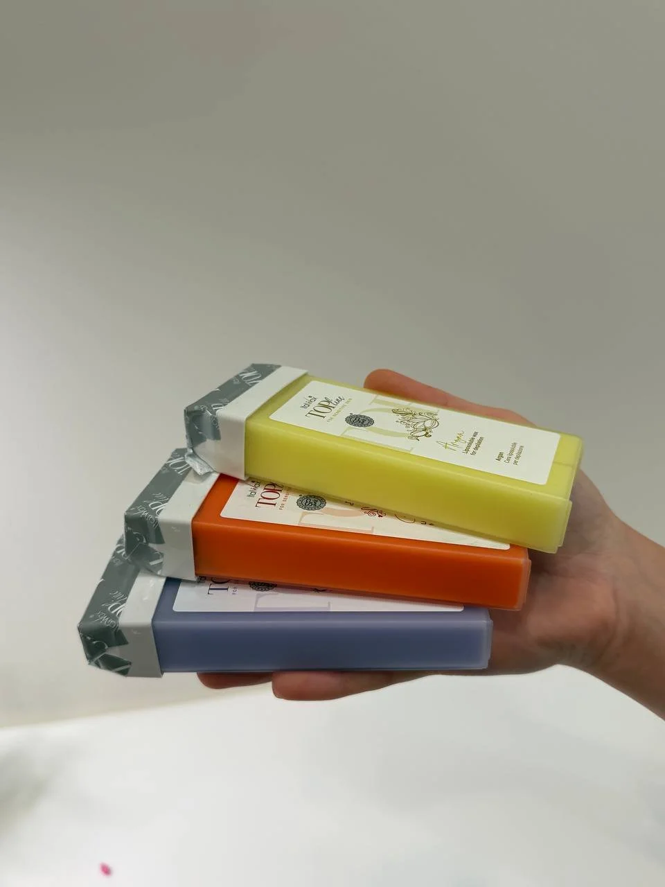 A hand holding three bars of colorful soap in yellow, orange, and blue.