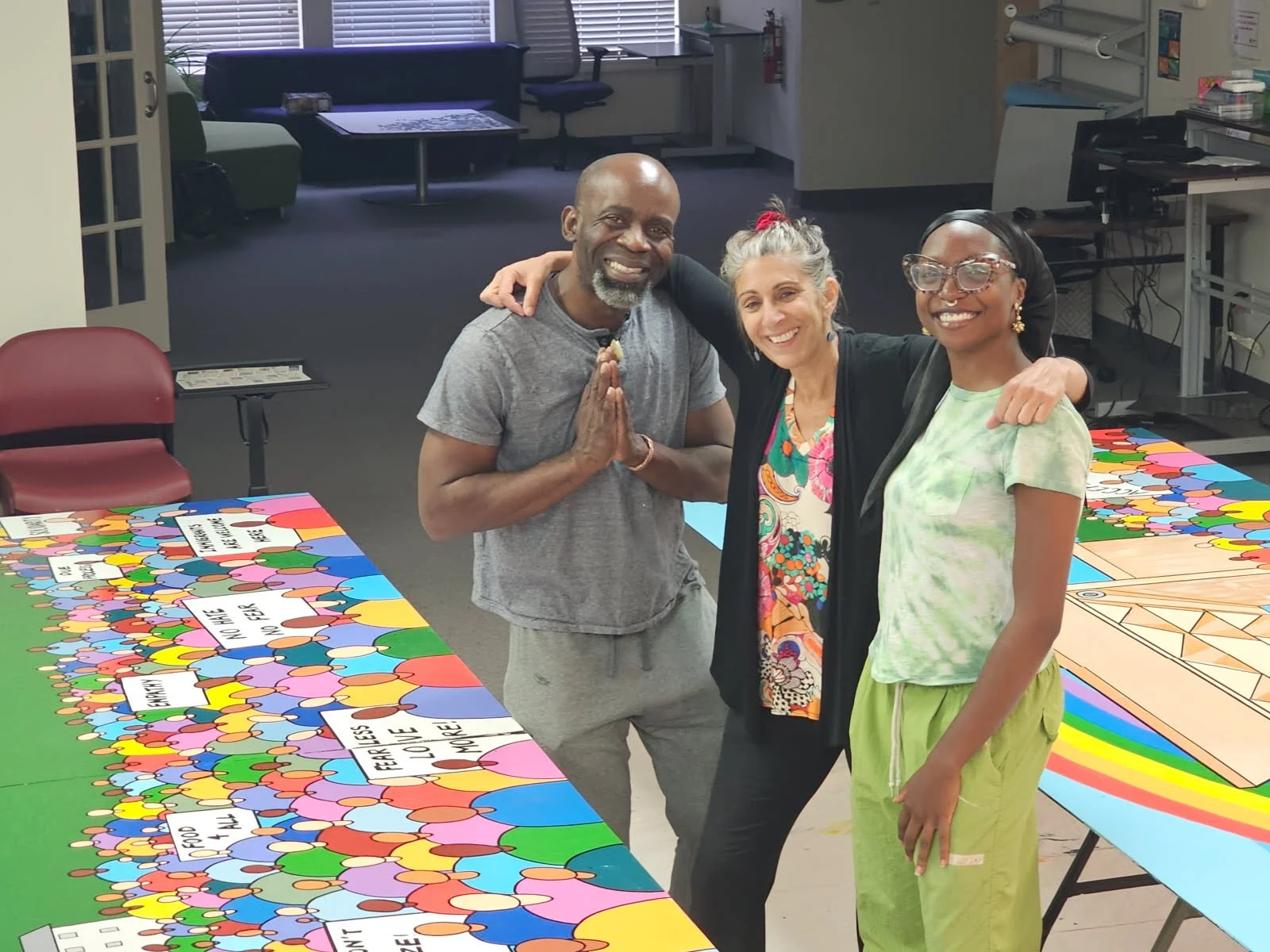 Raph Draws with two collaborators smiling in front of the colorful Why We March mural during the painting process, Burlington VT, 2025