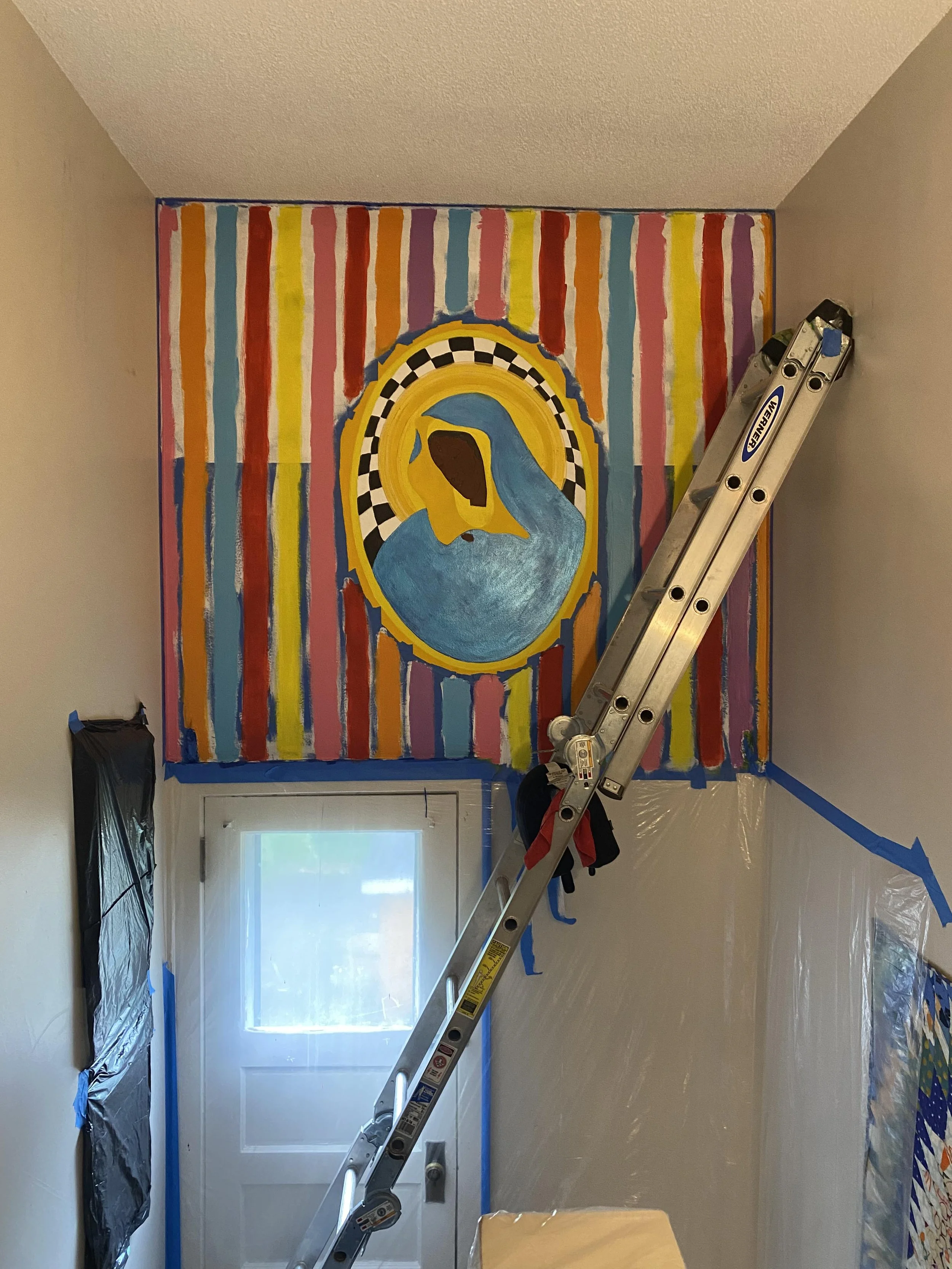 A mural in progress above a doorway showing a Black Madonna figure in a gold halo, now surrounded by bold vertical stripes in red, orange, yellow, teal, and pink across the full wall.