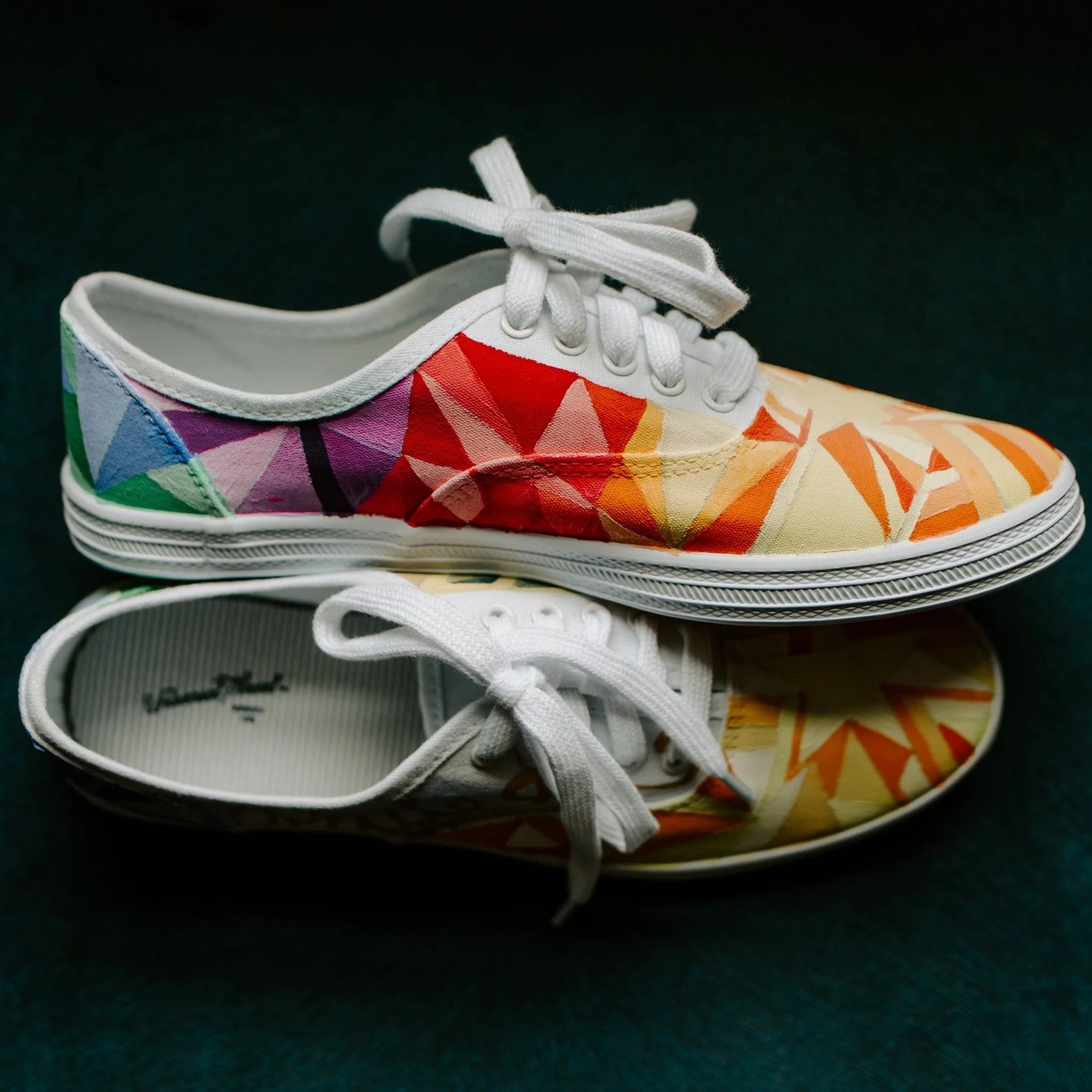 Pair of colorful sneakers with geometric patterns, one with a rainbow gradient and the other with orange and white designs, placed on top of each other.