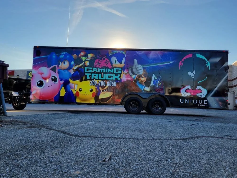 A gaming truck decorated with characters from popular video games, including Kirby, Sonic the Hedgehog, Pikachu, Donkey Kong, and others, parked on a parking lot.