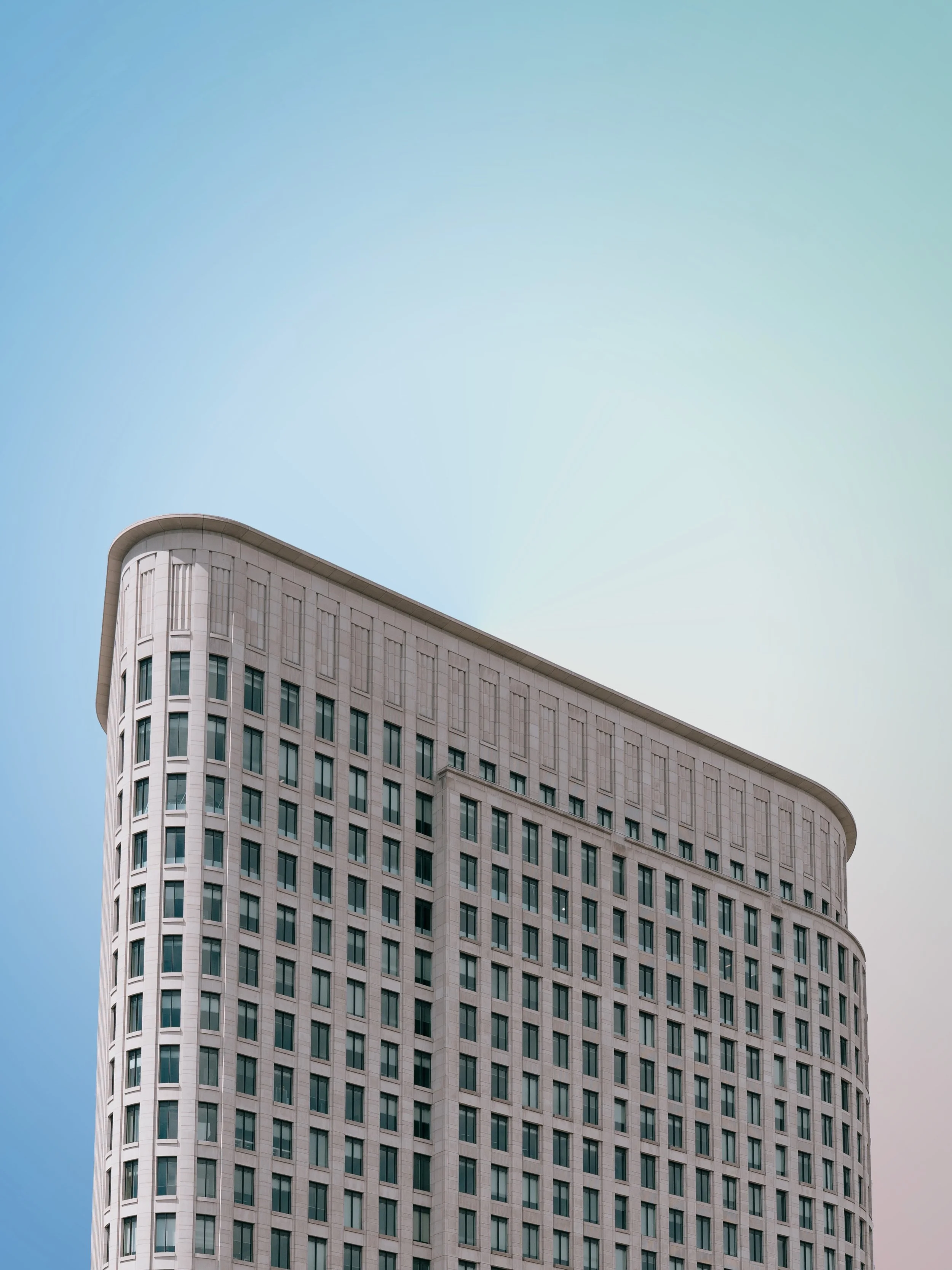 A tall modern office building with a curved facade and many windows, set against a clear sky with a gradient from blue to pale green.