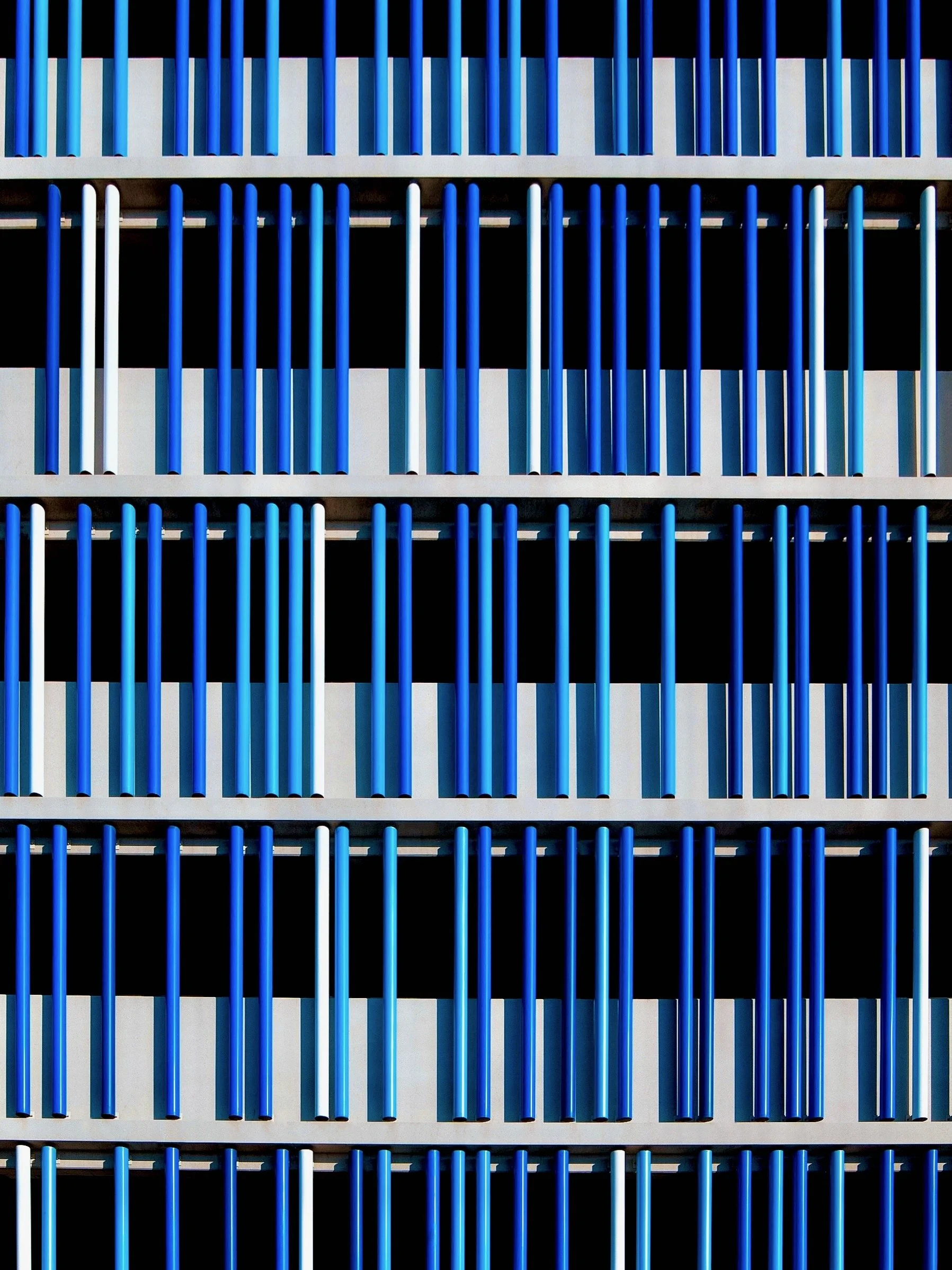 Close-up of a modern building facade with horizontal rows of blue and white vertical bars and black background.