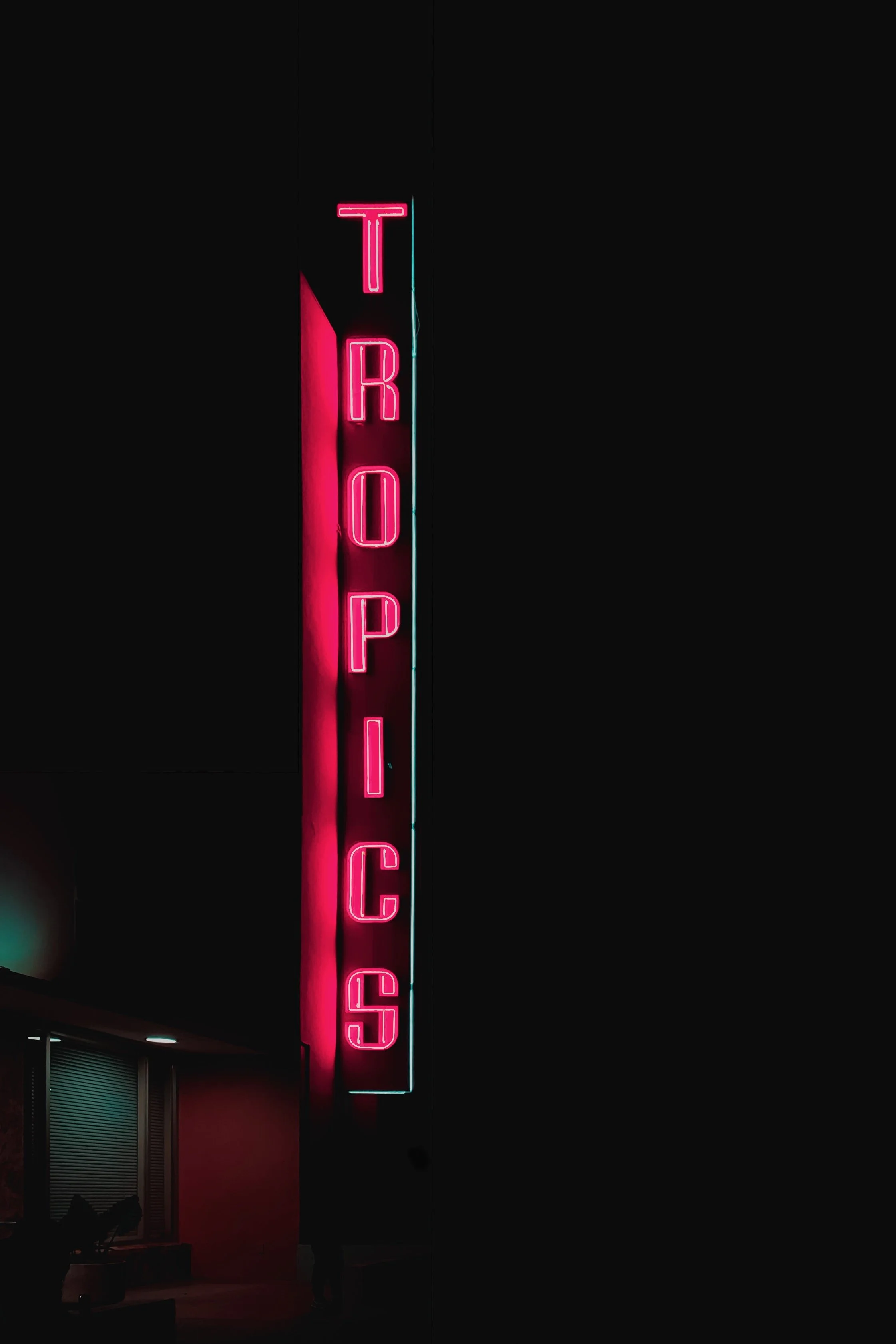 Vertical neon pink 'TROPHIC' sign on a building at night with a dark sky background.