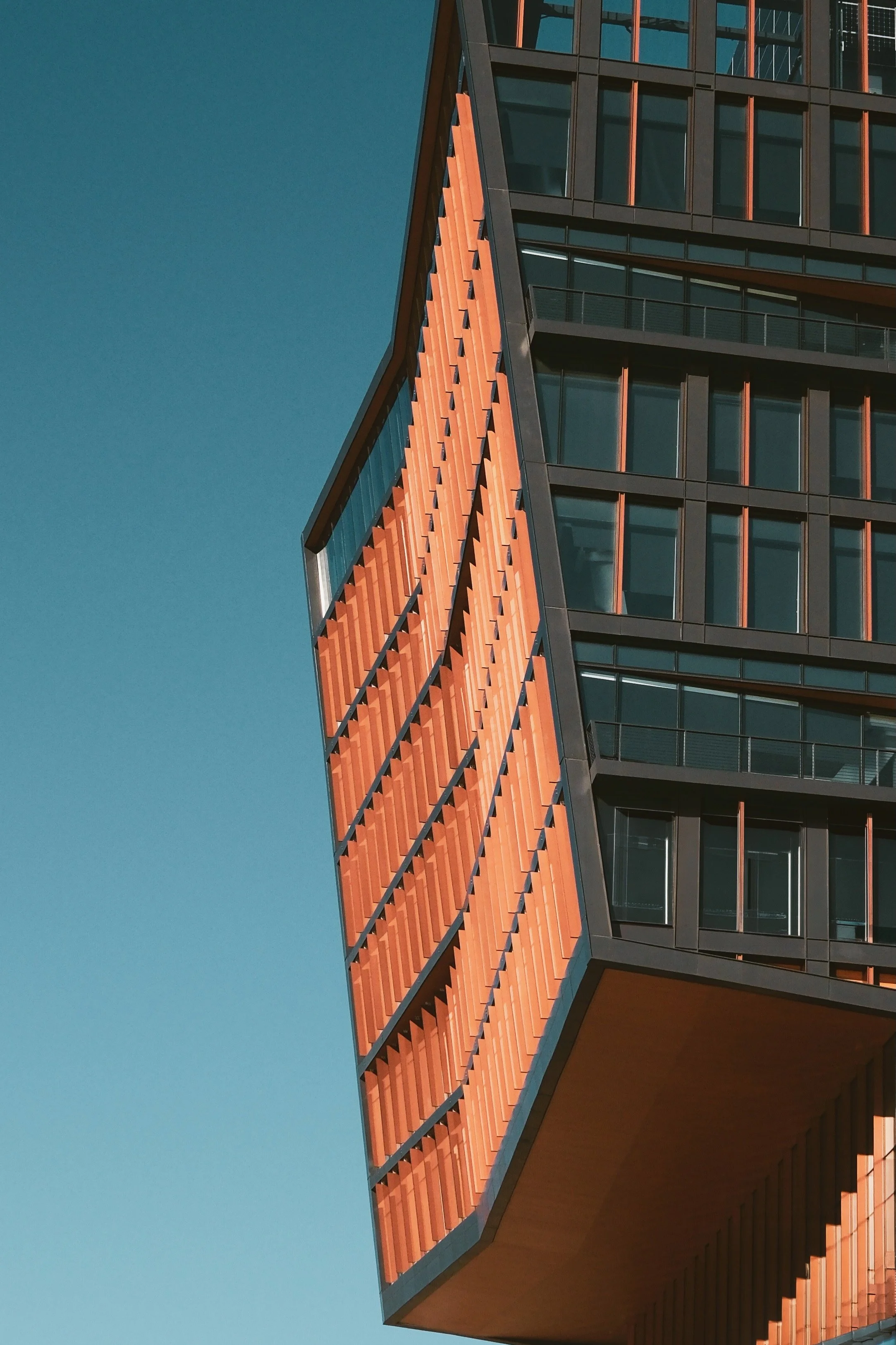 Close-up of a modern building with orange and black paneling and glass windows against a clear blue sky.