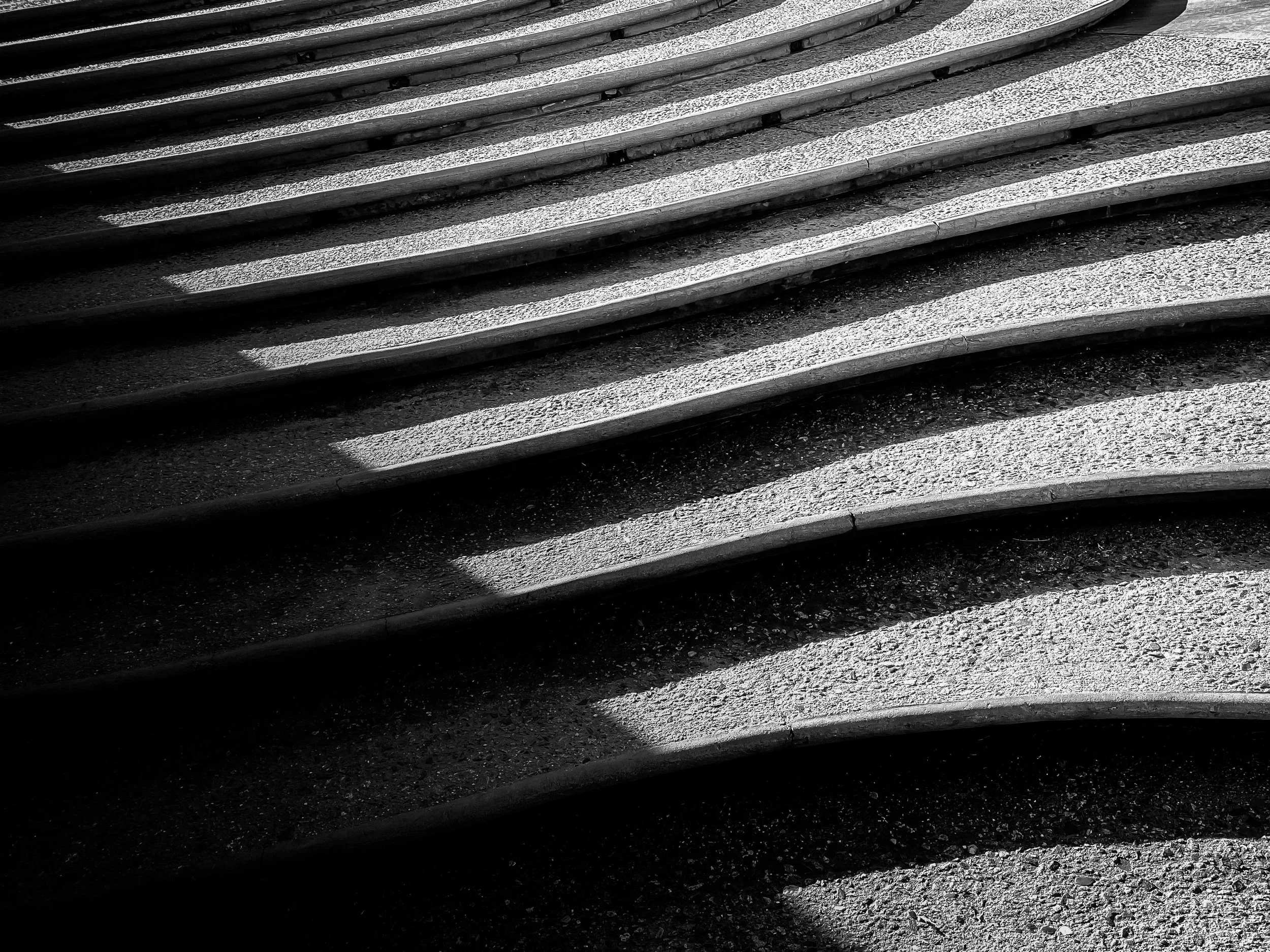 Close-up of concrete stairs casting shadows on the ground in black and white.