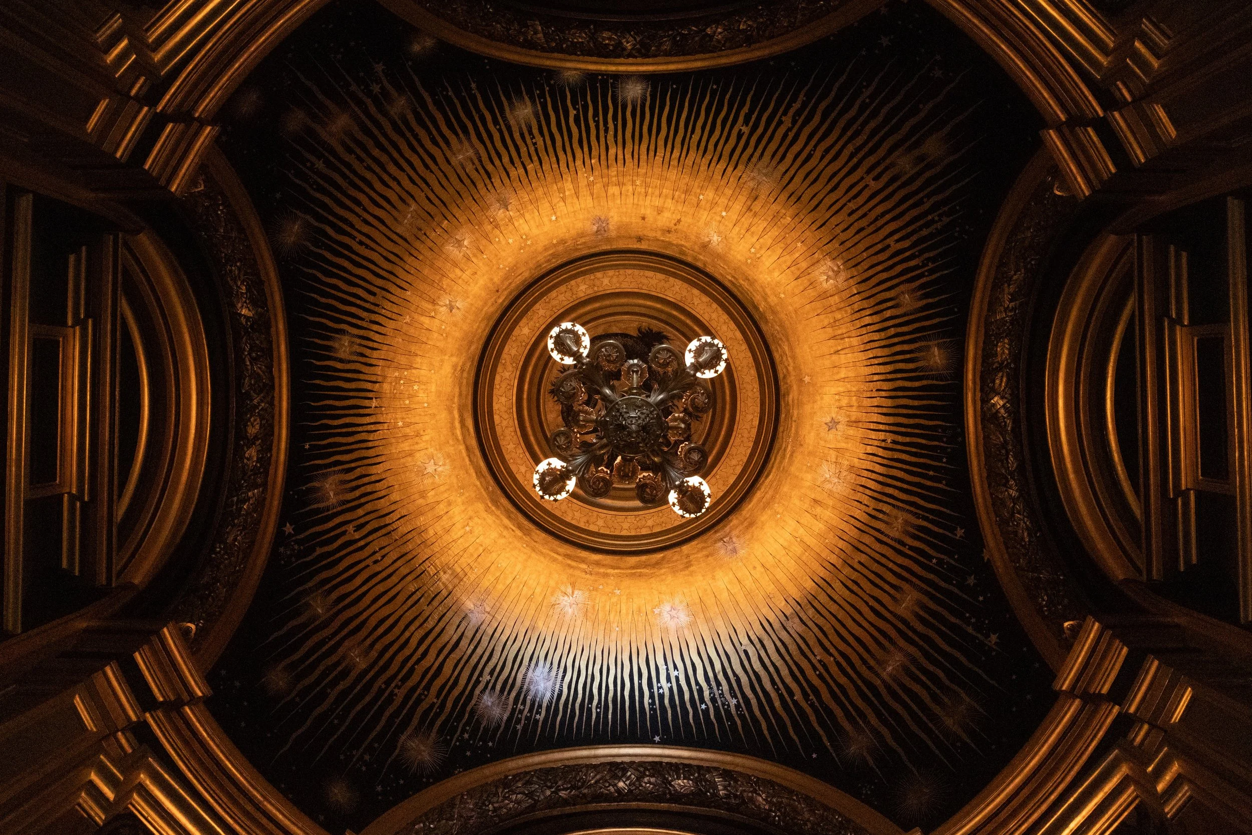 Decorative chandelier hanging from an ornate ceiling with gold accents and star motifs.