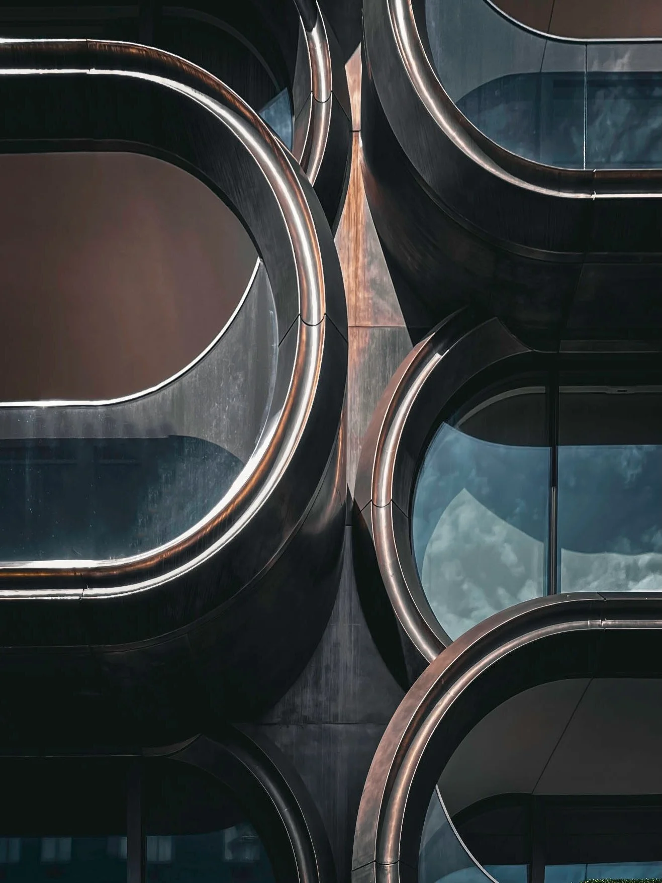 Aerial view of modern building with rounded glass windows and metallic edges reflecting light.