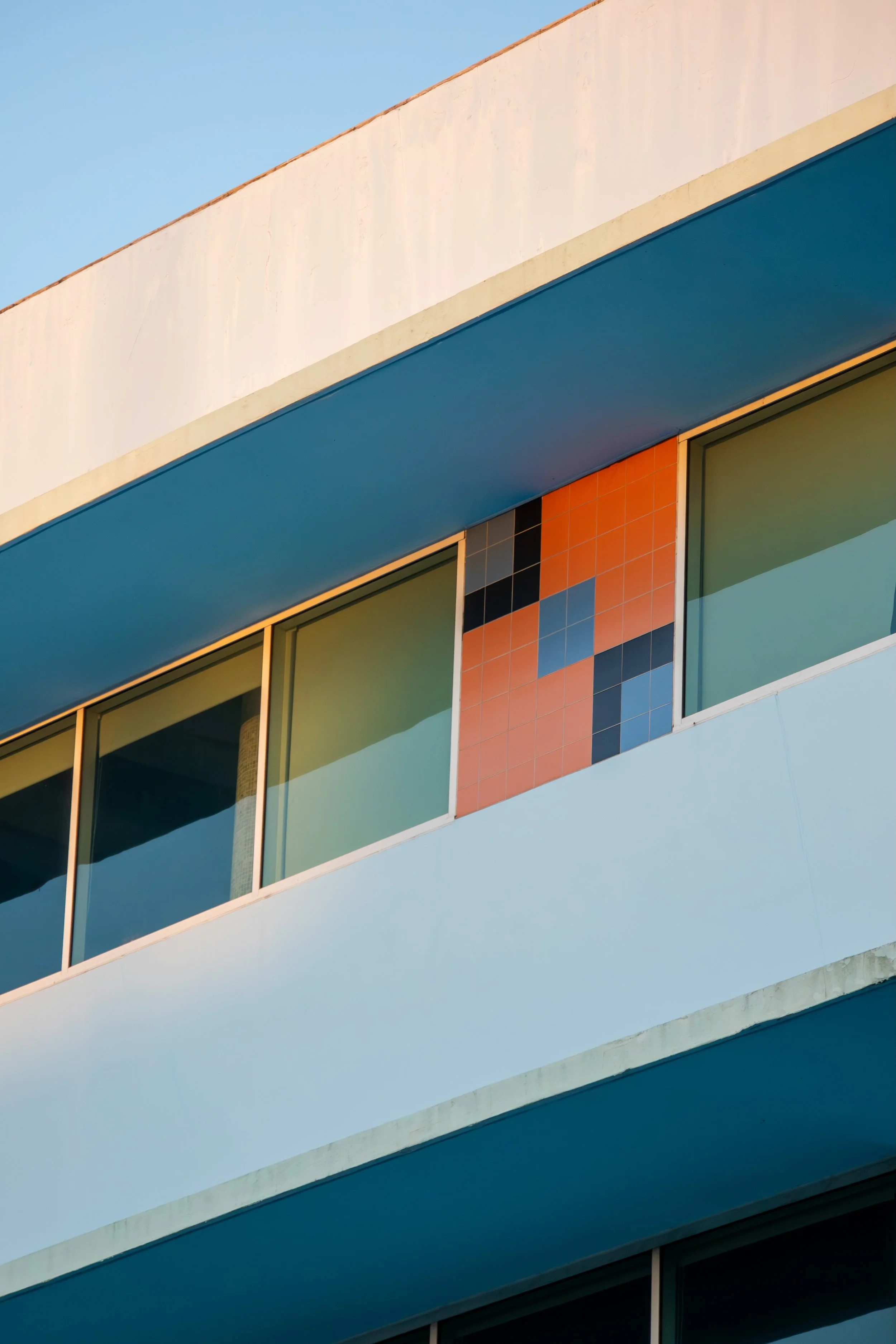 Close-up of a modern building's exterior, featuring colorful tiled accents and large glass windows under a clear blue sky.