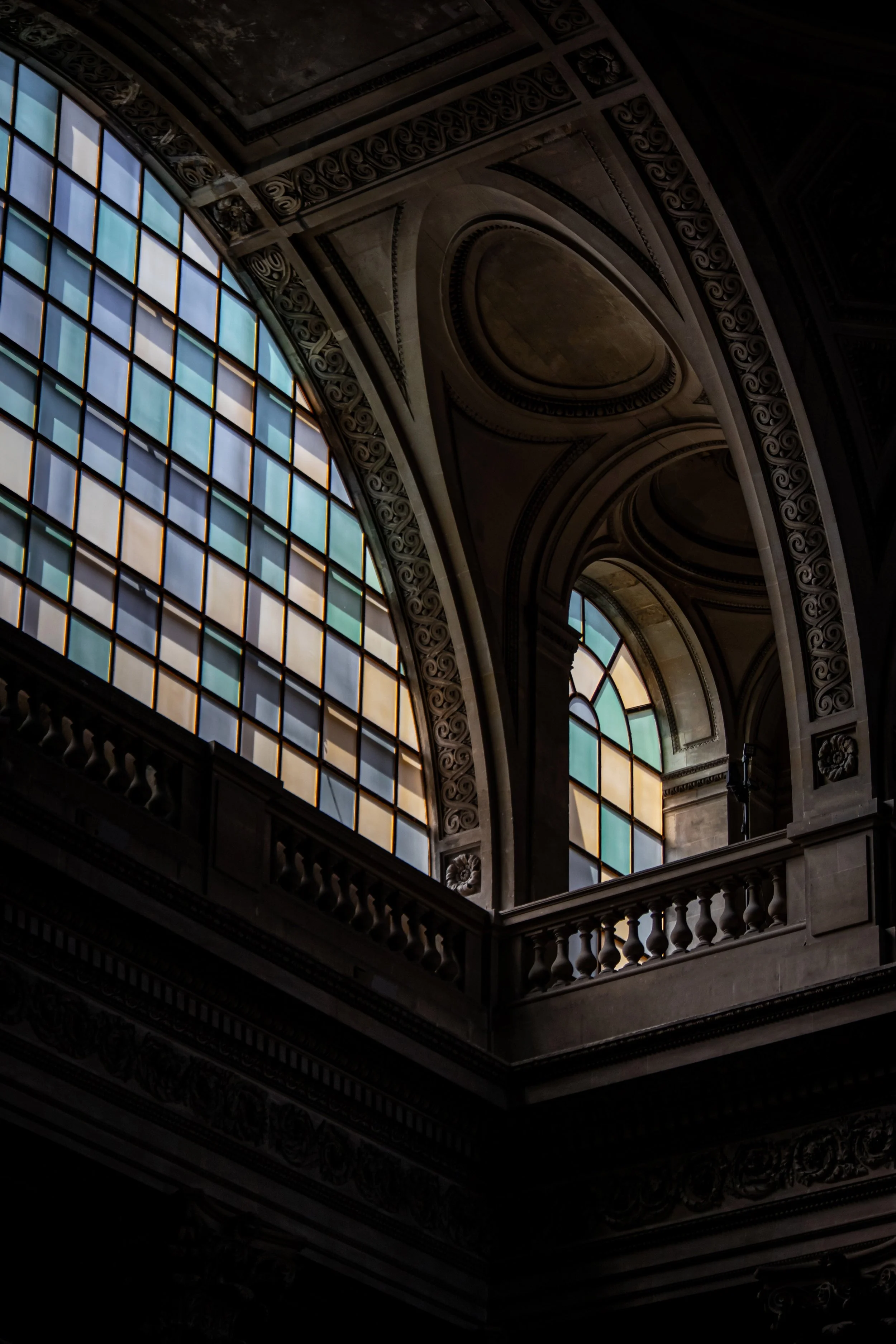 Interior view of a historic building with large stained glass windows, ornate ceiling moldings, and a decorative balustrade.