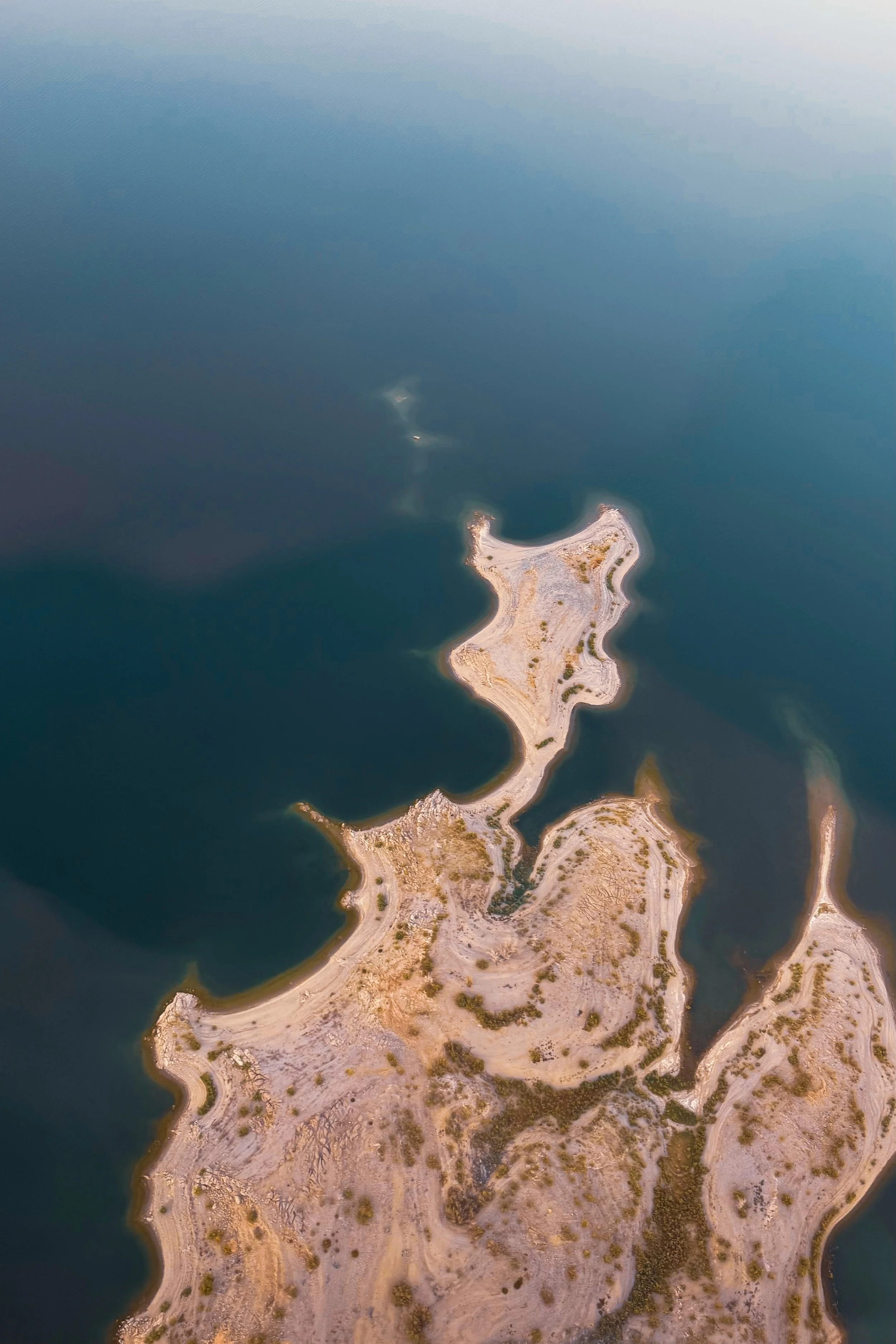 An aerial view of a small, rocky island with rugged terrain, surrounded by a calm, blue body of water.