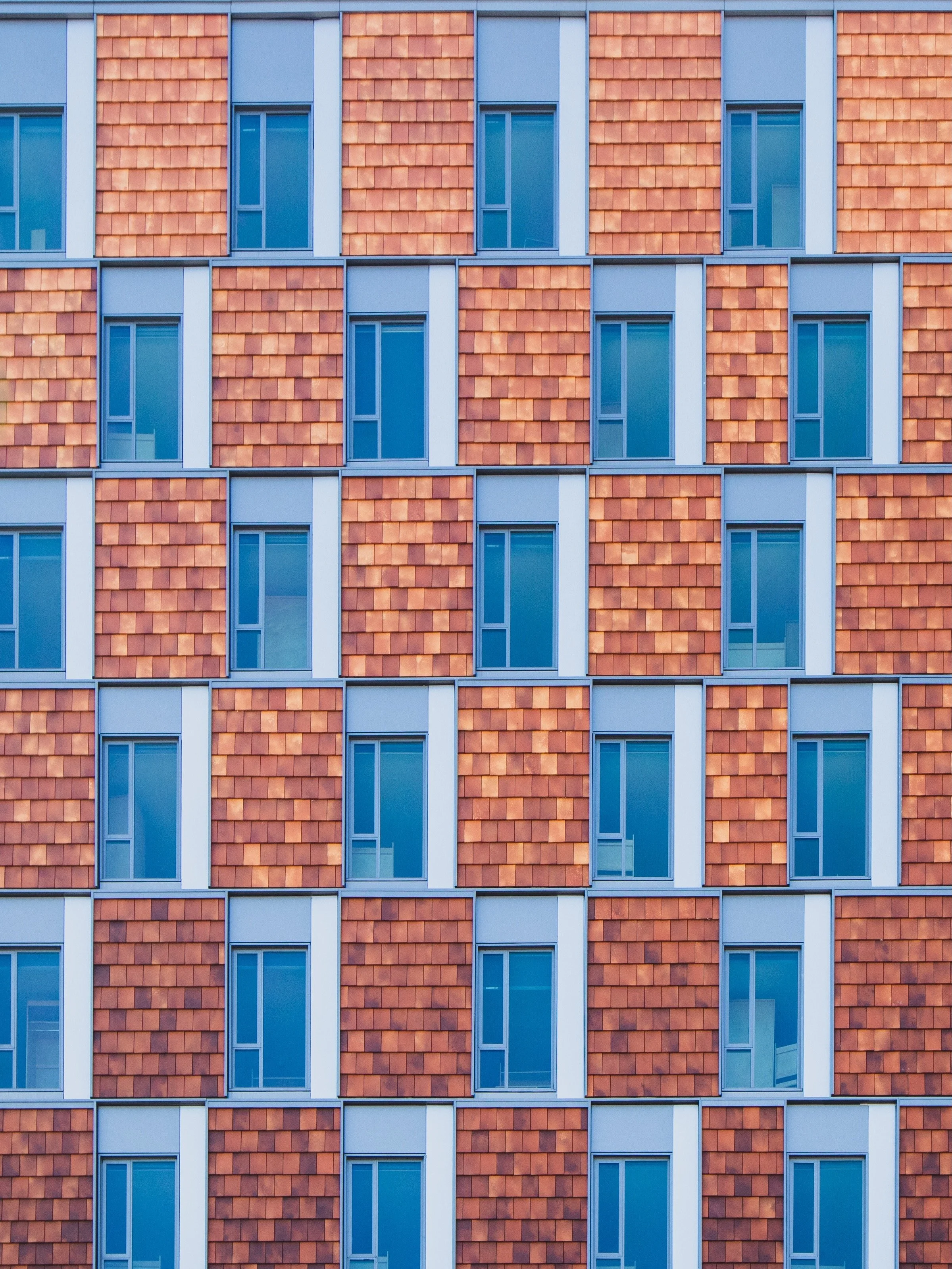 A building facade with a grid of windows and red brick-patterned panels in alternating rows.