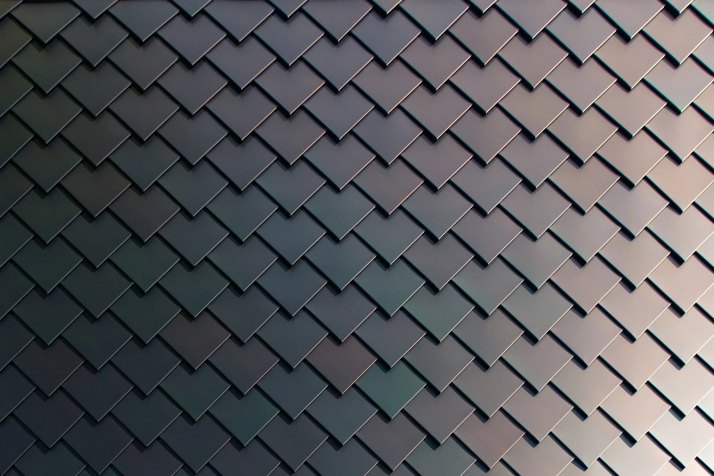 Close-up of a dark metal wall with overlapping diamond-shaped tiles arranged in a grid pattern.