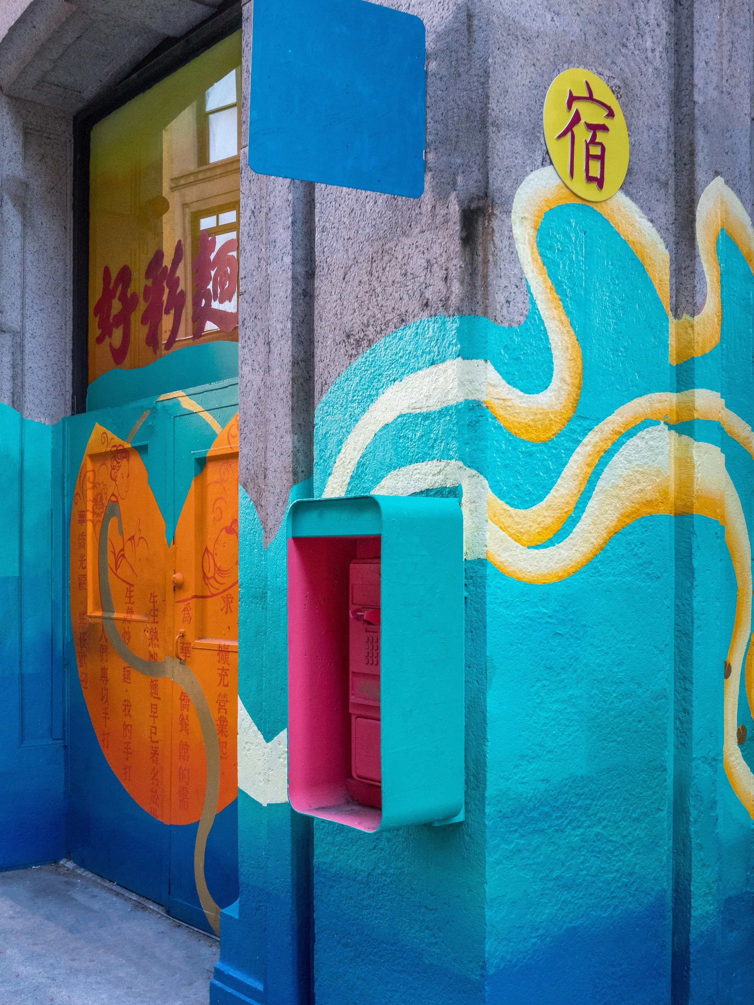 Colorful mural with Chinese characters, a decorative octopus, and a pink mailbox on a gray building wall.