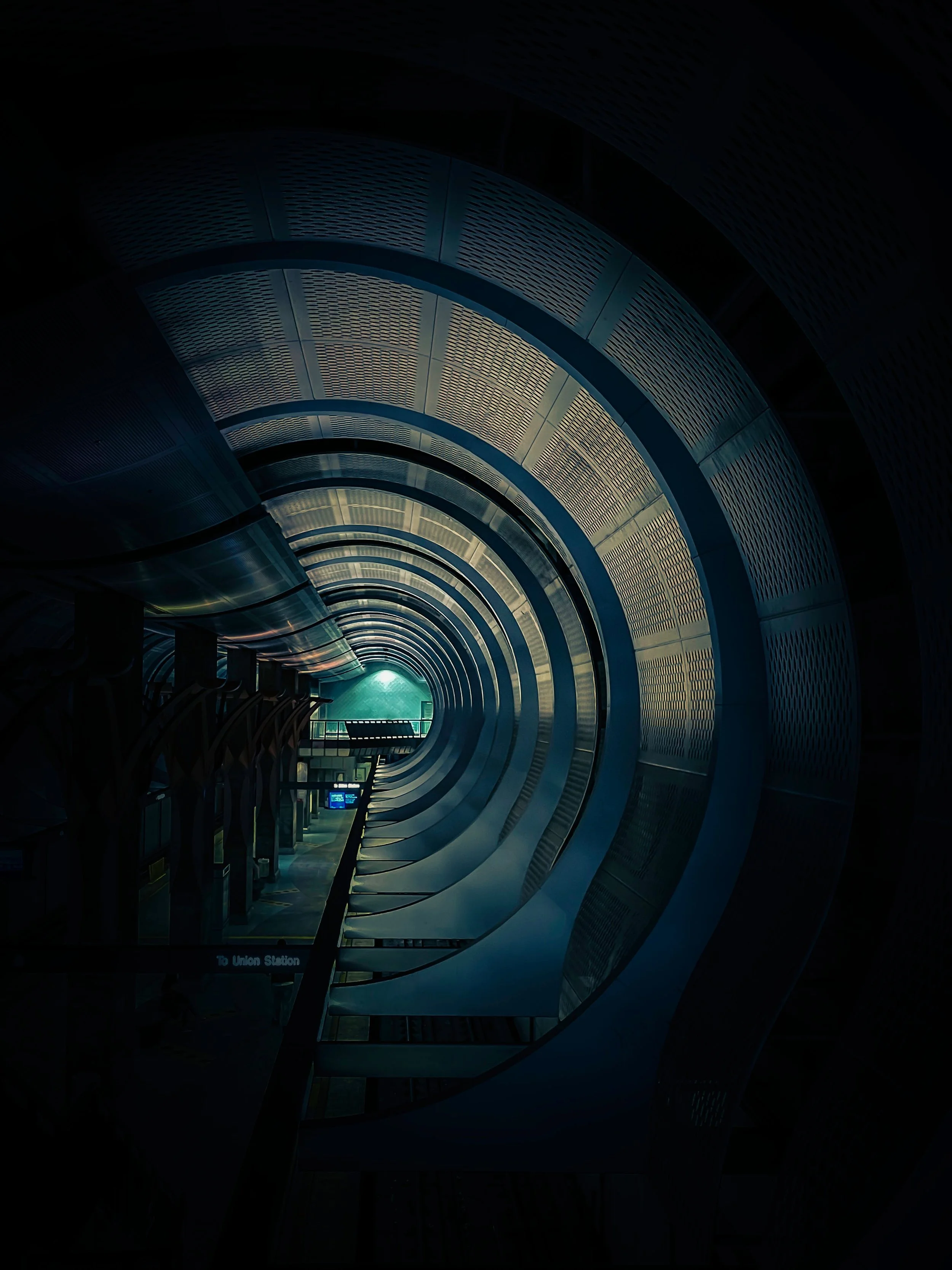 Modern enclosed train or bus station with circular tunnel-like design, illuminated at the end with a blue hue.