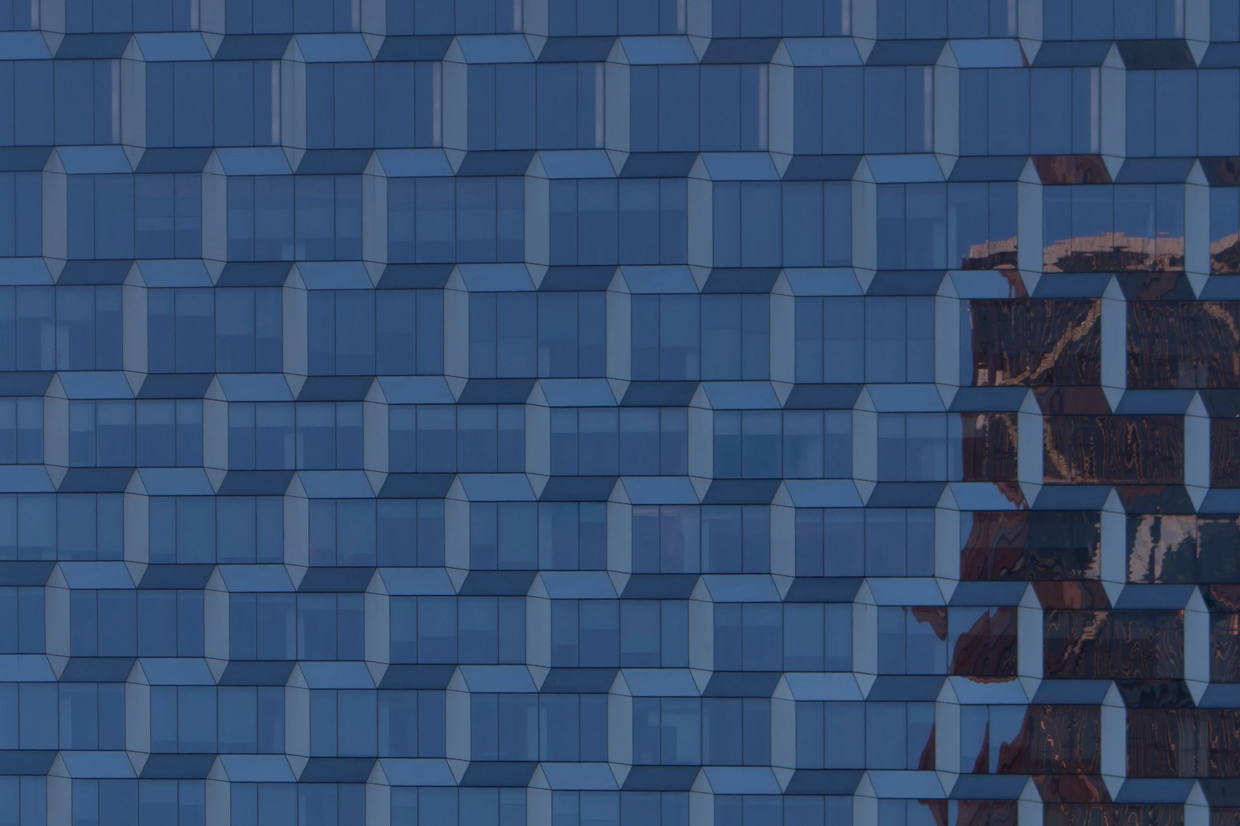 Close-up of a modern building's facade with reflective glass windows showing geometric patterns and reflections of neighboring buildings.