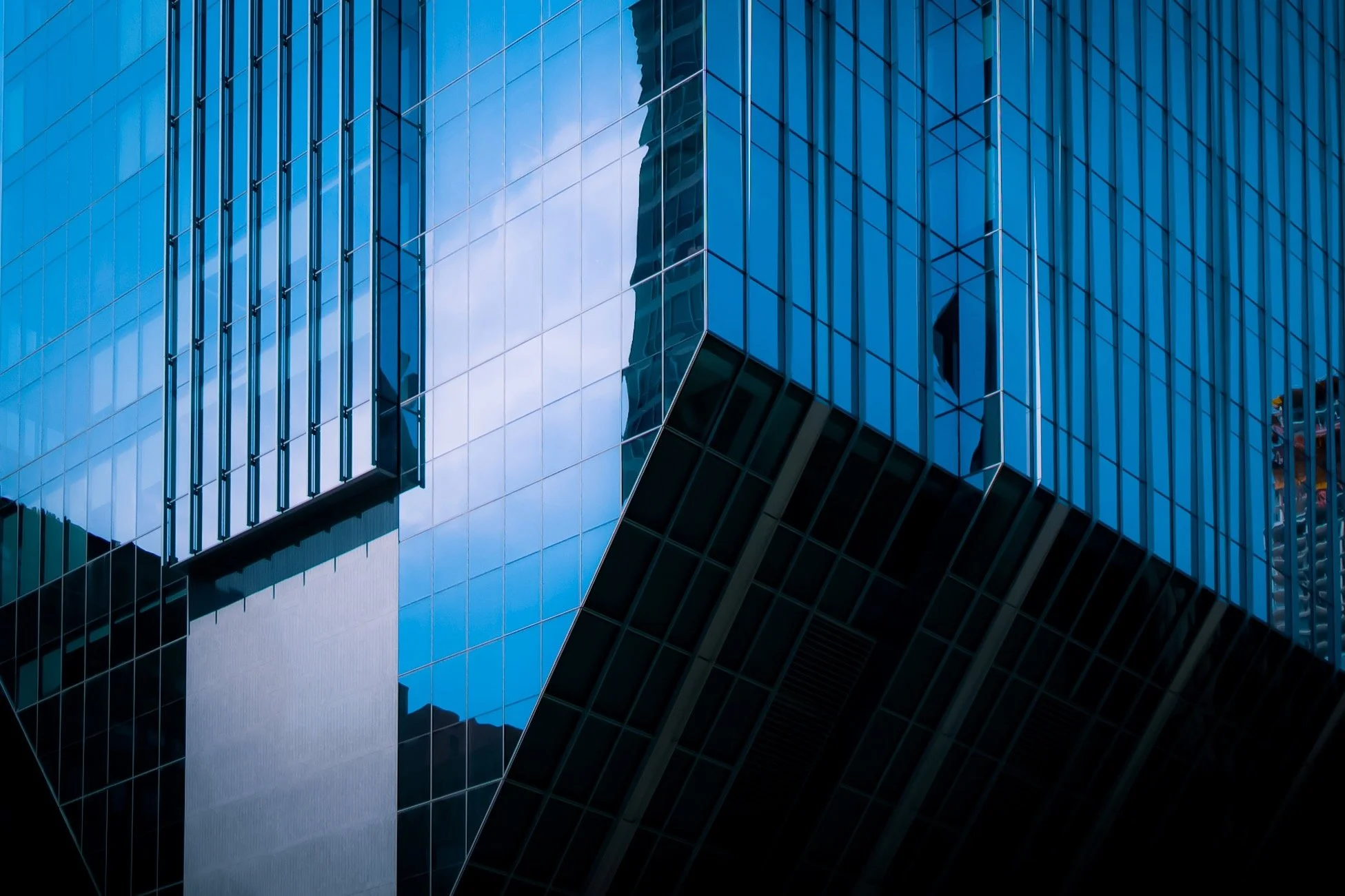 Close-up view of a modern glass skyscraper with reflective blue windows and geometric architectural design.