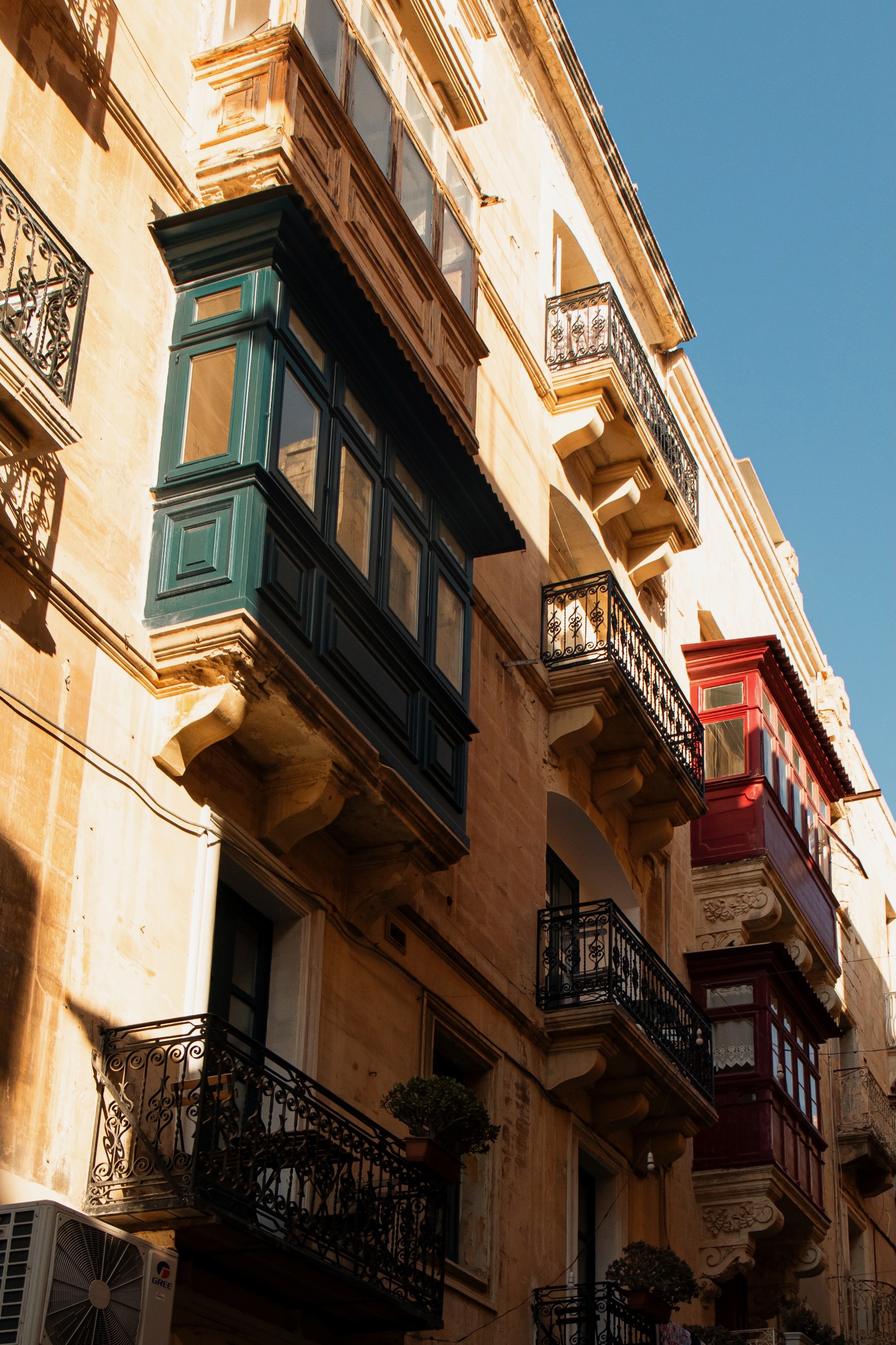 Multiple ornate balconies with colorful enclosed porches on a historic building under a clear blue sky.