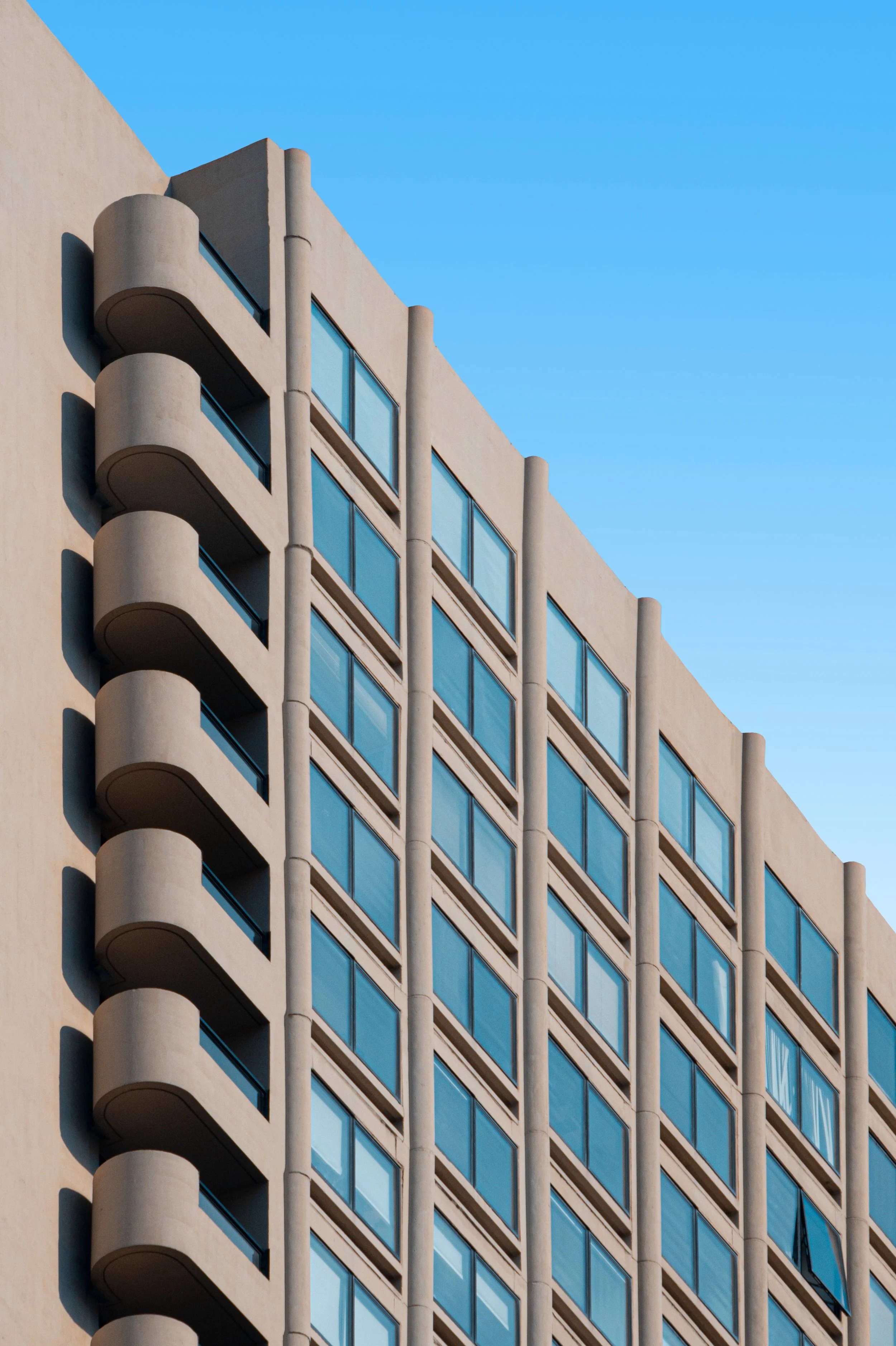 A modern high-rise building with rounded balconies on its corner and many windows, against a blue sky.
