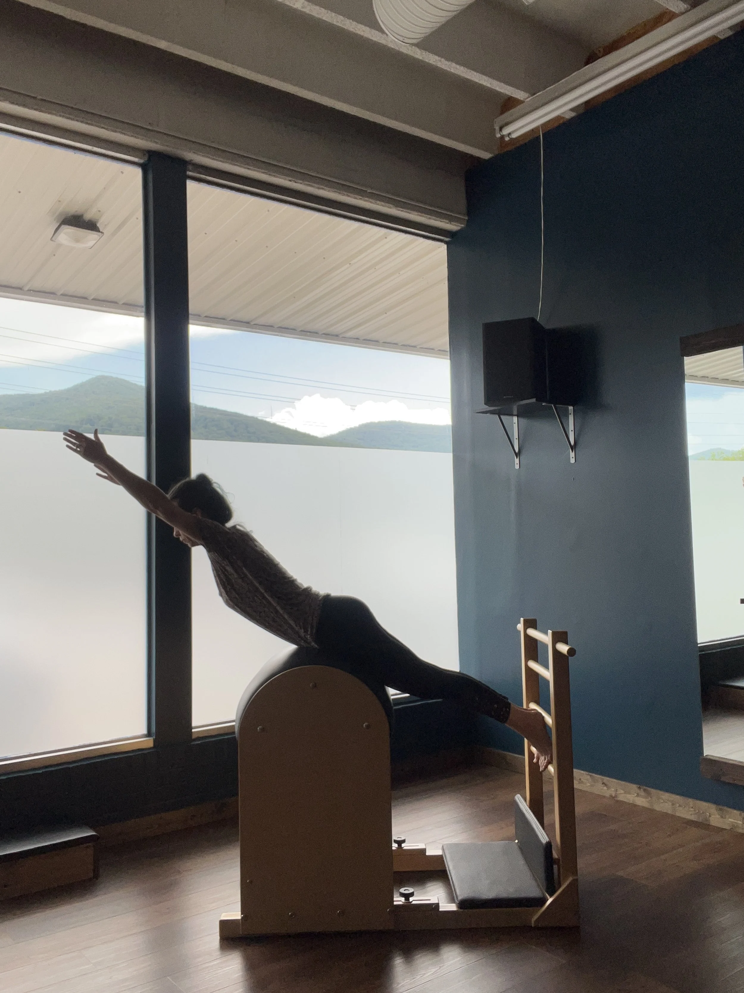 A person practicing Pilates on a ladder barrel near large windows with mountain views.