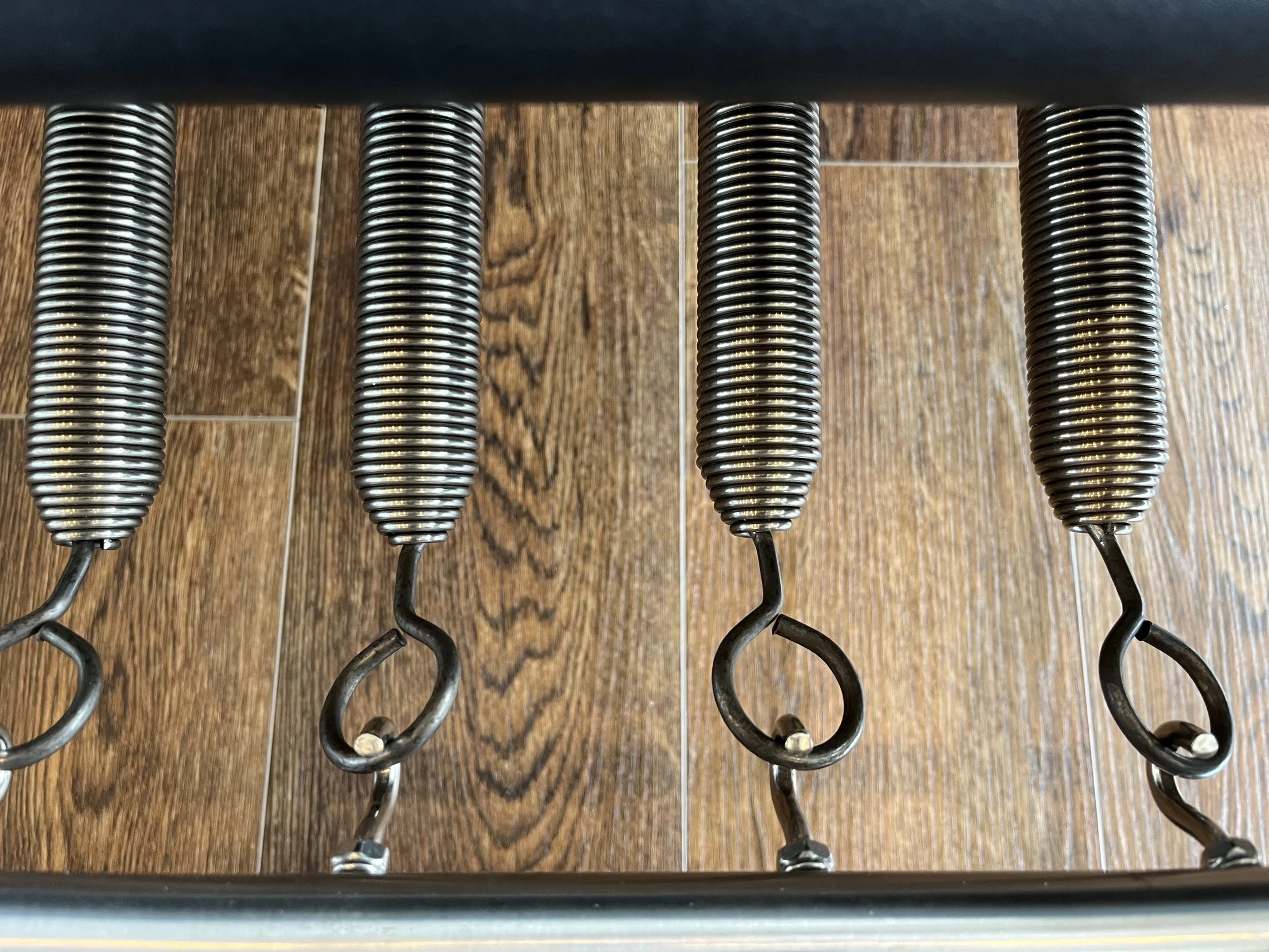Close-up of four metal footrests with coiled springs, mounted on a black surface, on a wooden floor.
