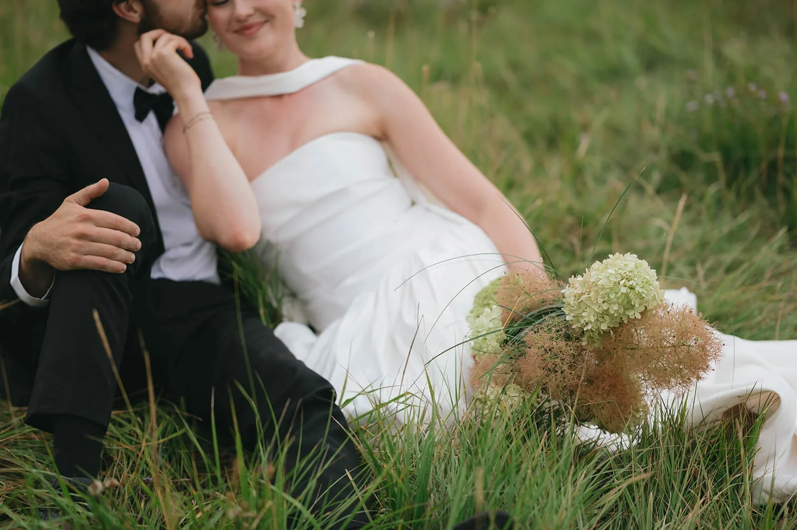 Bride with modern bridal bouquet and groom cuddle in open mountain field outside of Bend Oregon on elopement day