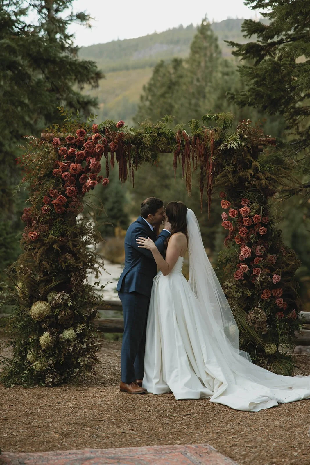 bride and groom kiss under artful flower arch in Bend Oregon