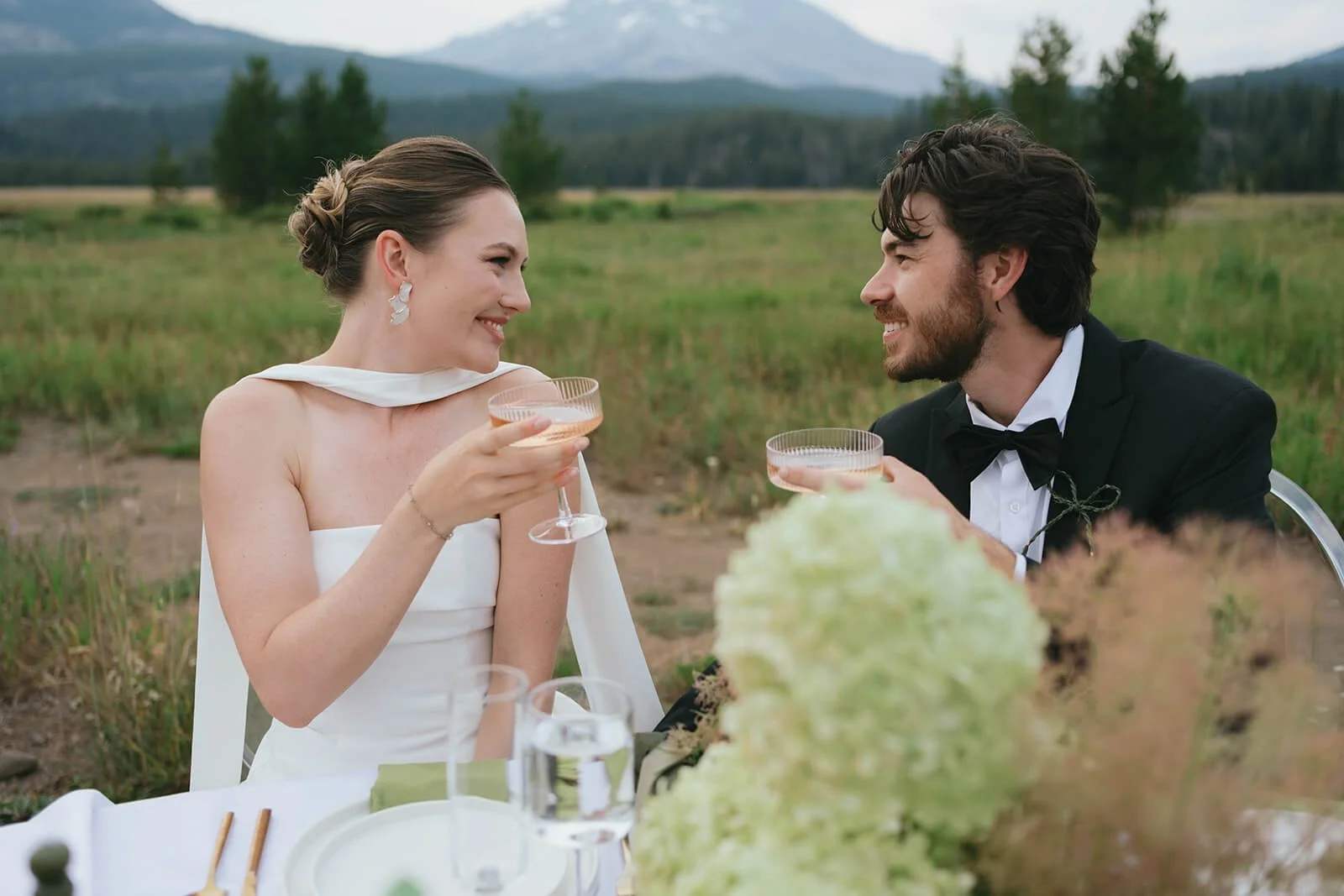 bride and groom share sparkling rose at there elopement dinner in the mountains. Green and nude floral arrangements by SlowCult floral studio in foreground