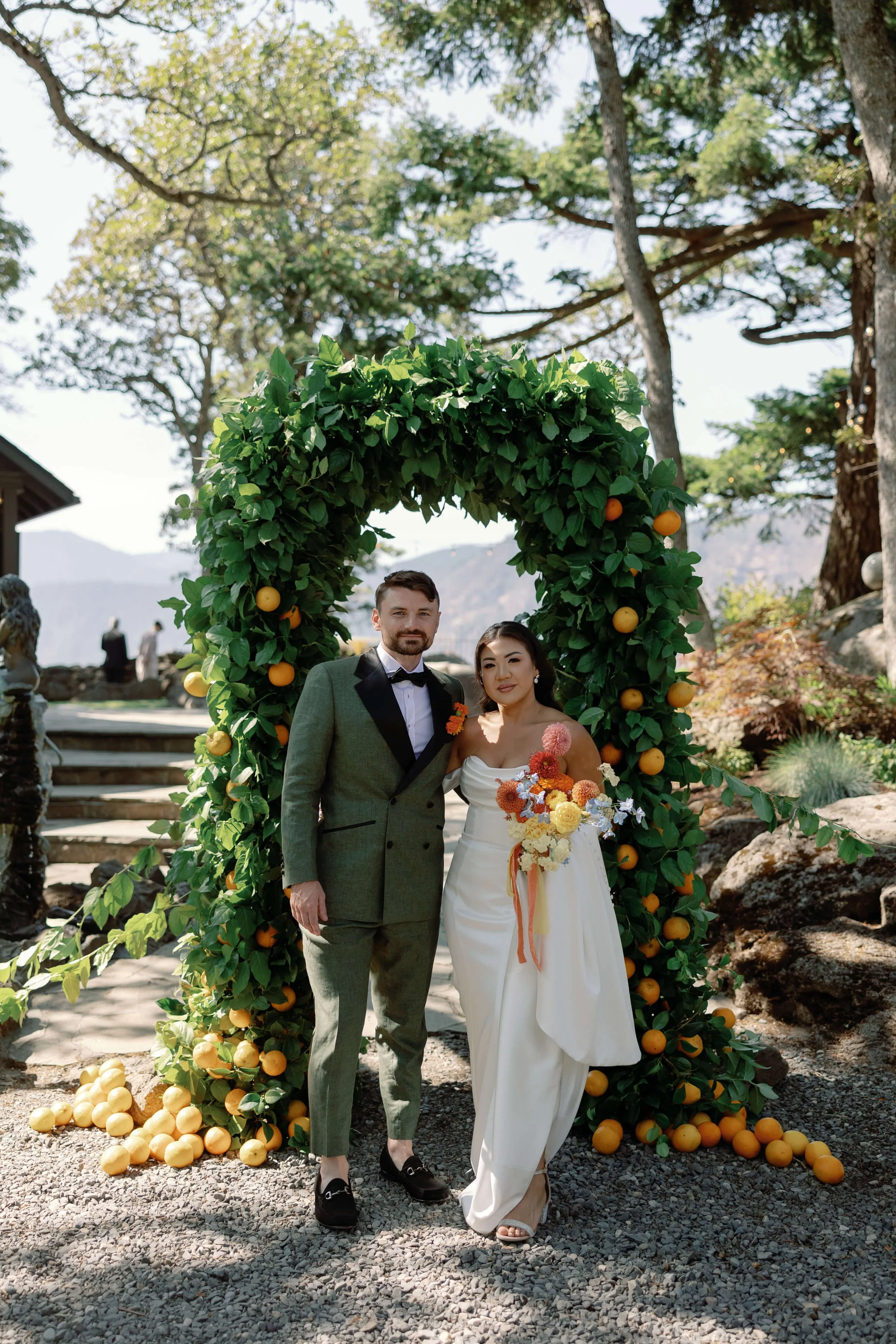 contemporary bride holding colorful bouquet and groom stand infant of orange floral arch Griffin House Oregon