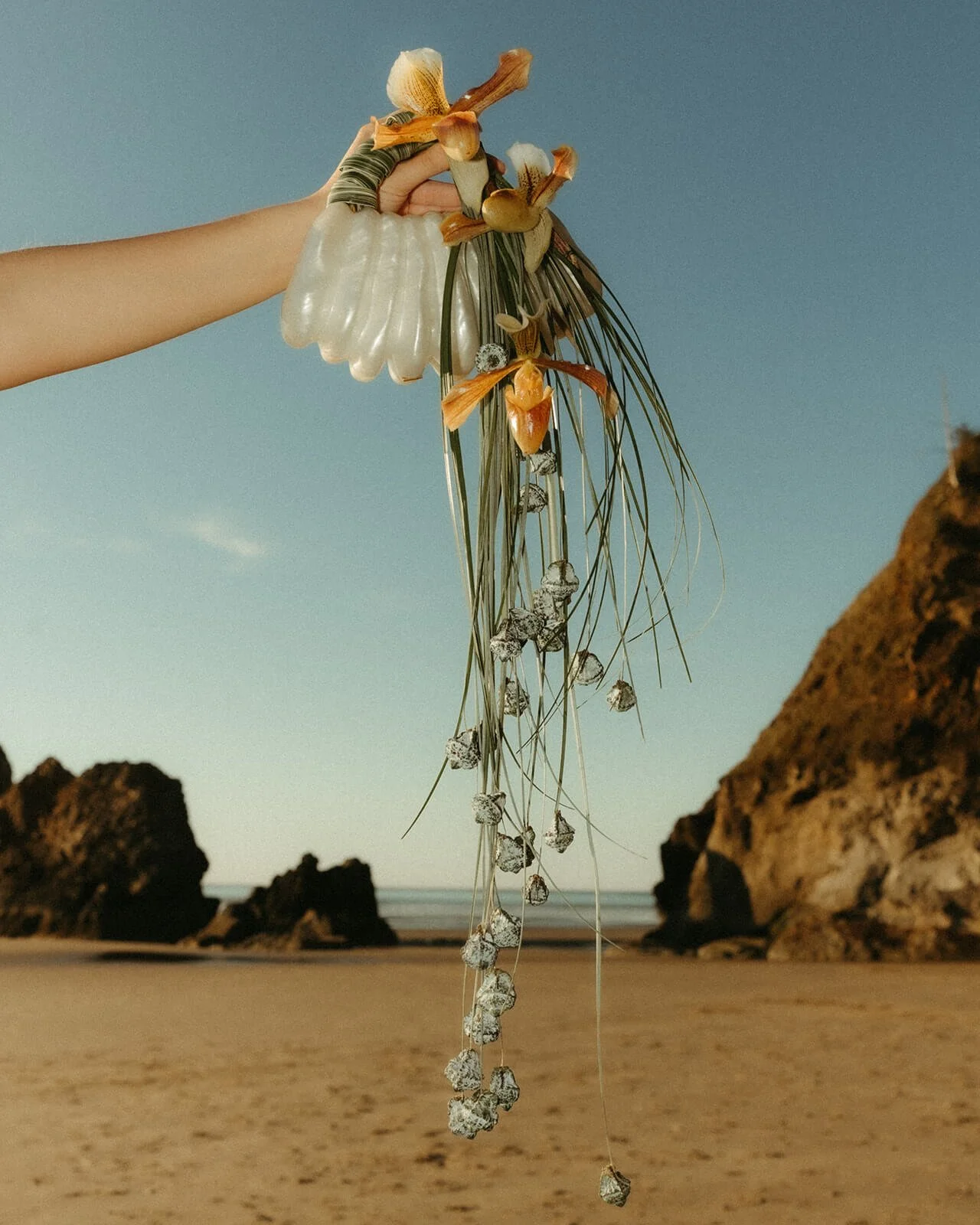 Contemporary bridal accessory shell back with hanging florals and orchids against coastal backdrop