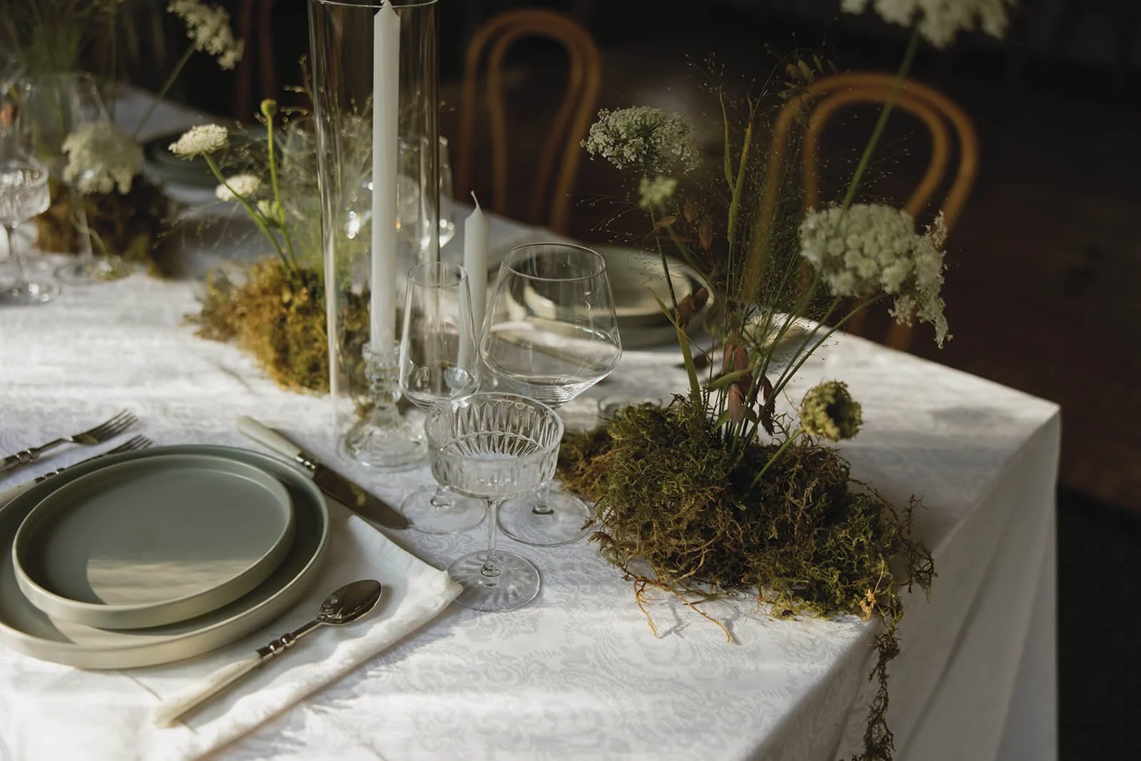 wedding reception table moss mounds with wild white flowers run down the tables. explosion grass, ferns, candles, dinnerware at wedding reception