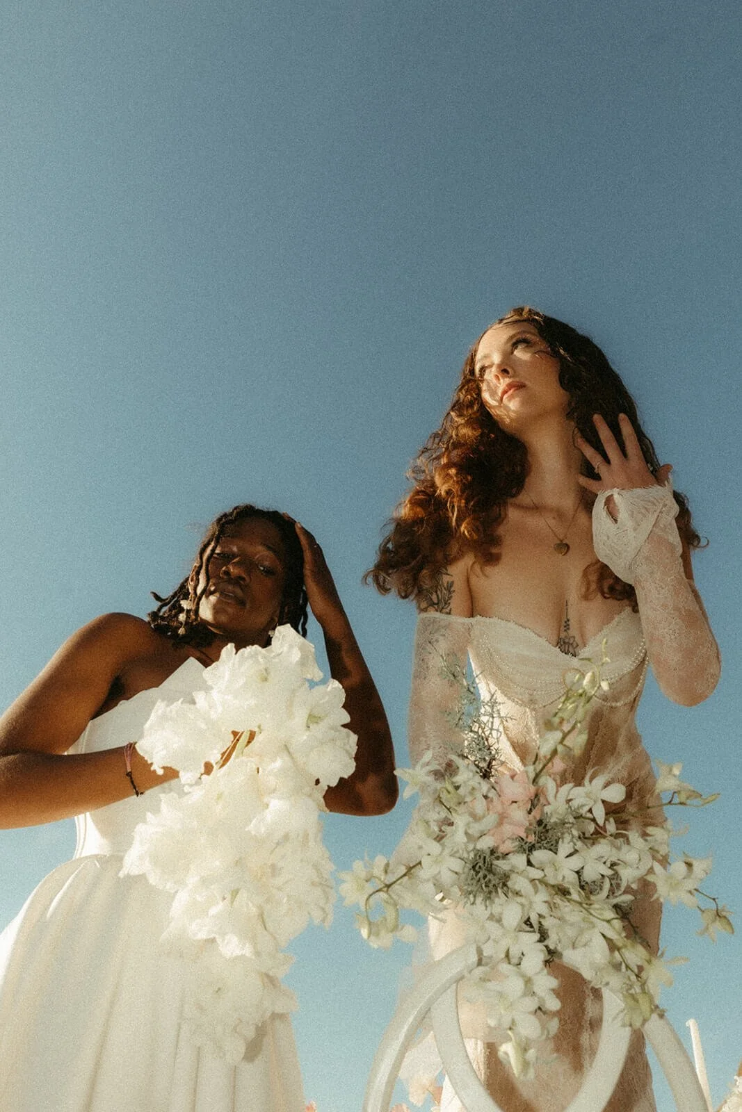 Two brides pose together with the sky as the background holding modern bridal bouquets