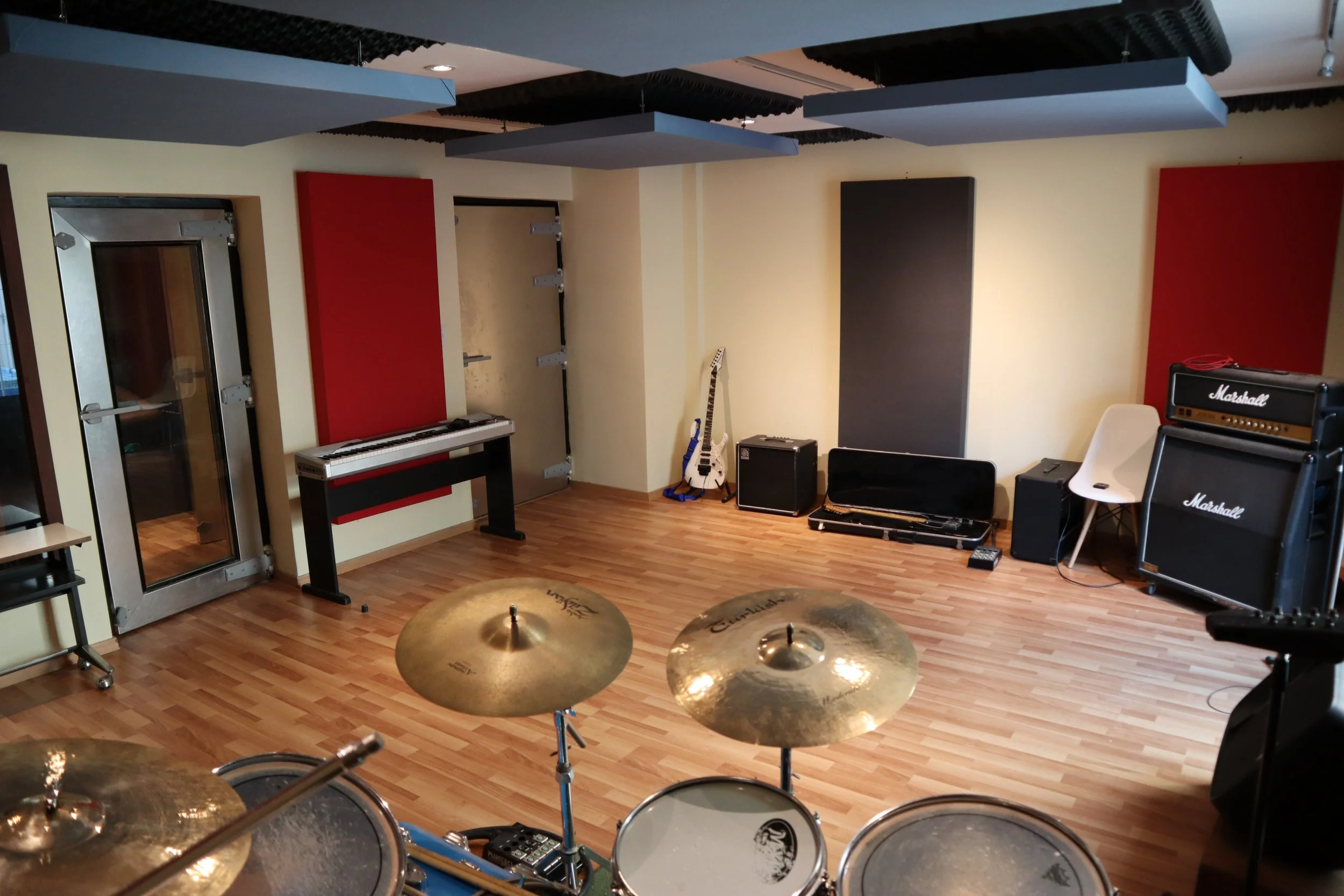 Sala de ensayo musical con diversos instrumentos como batería, guitarra, teclado y amplificadores en un estudio.