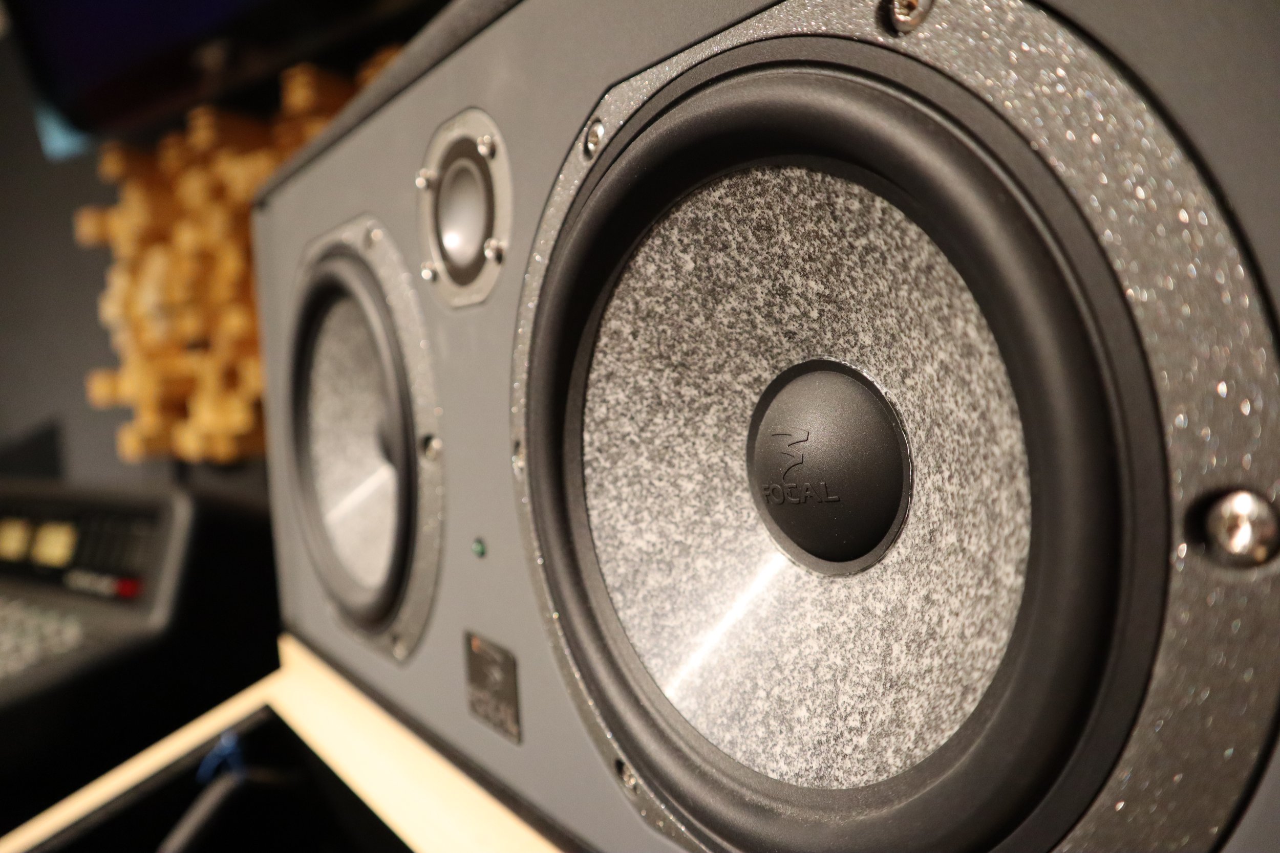 Altavoz de estudio Focal en un entorno de grabación, con fondo de material acústico y control remoto a la izquierda.