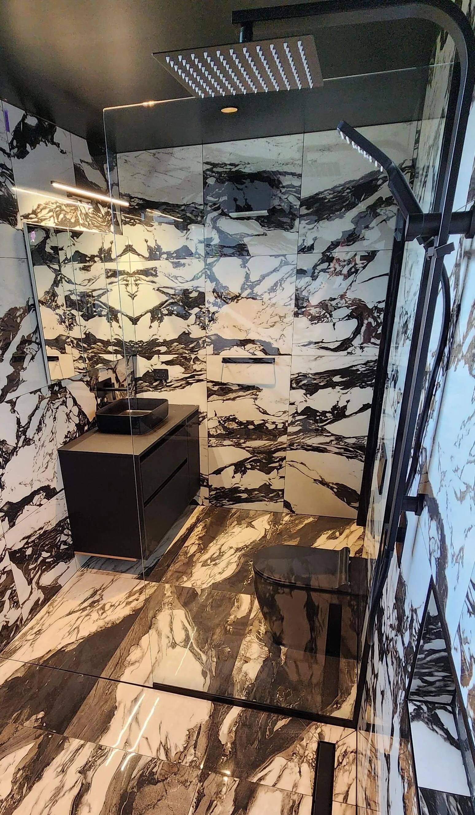 Luxury bathroom renovation in Dunedin featuring bold marble tiling, freestanding black bathtub, black toilet, and walk-in glass shower