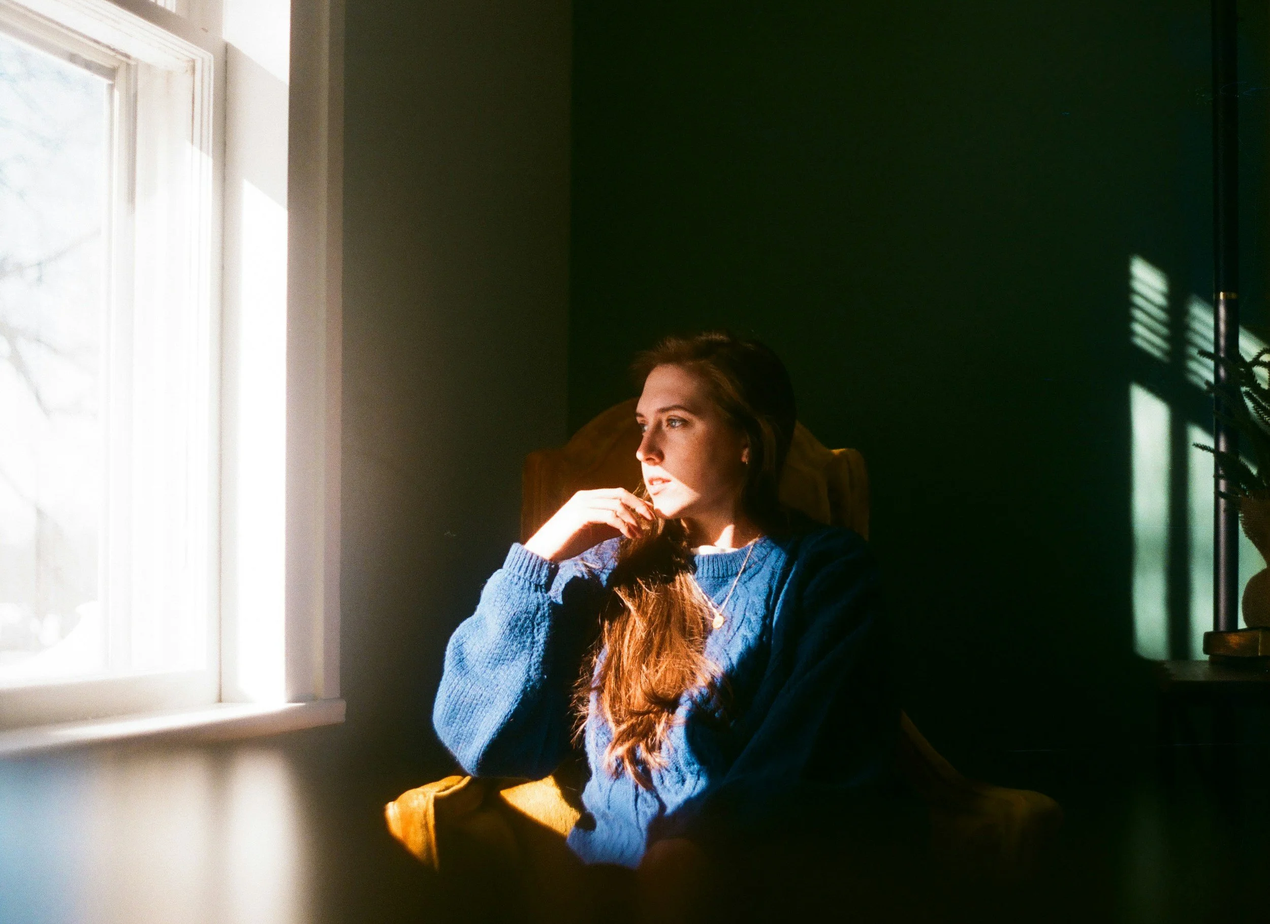 Adult sitting quietly by a window, reflecting on family patterns and intergenerational trauma.